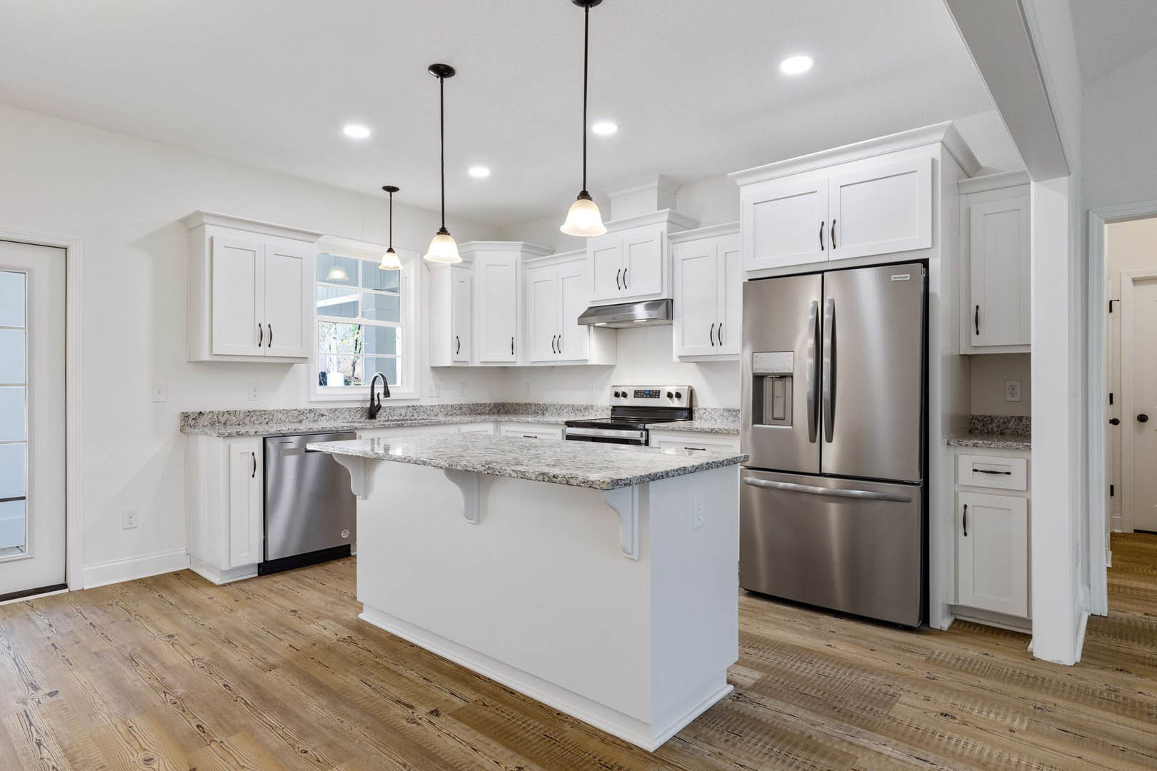 Spacious kitchen featuring a white island with granite countertops, stainless steel refrigerator, built-in oven, and modern cabinetry