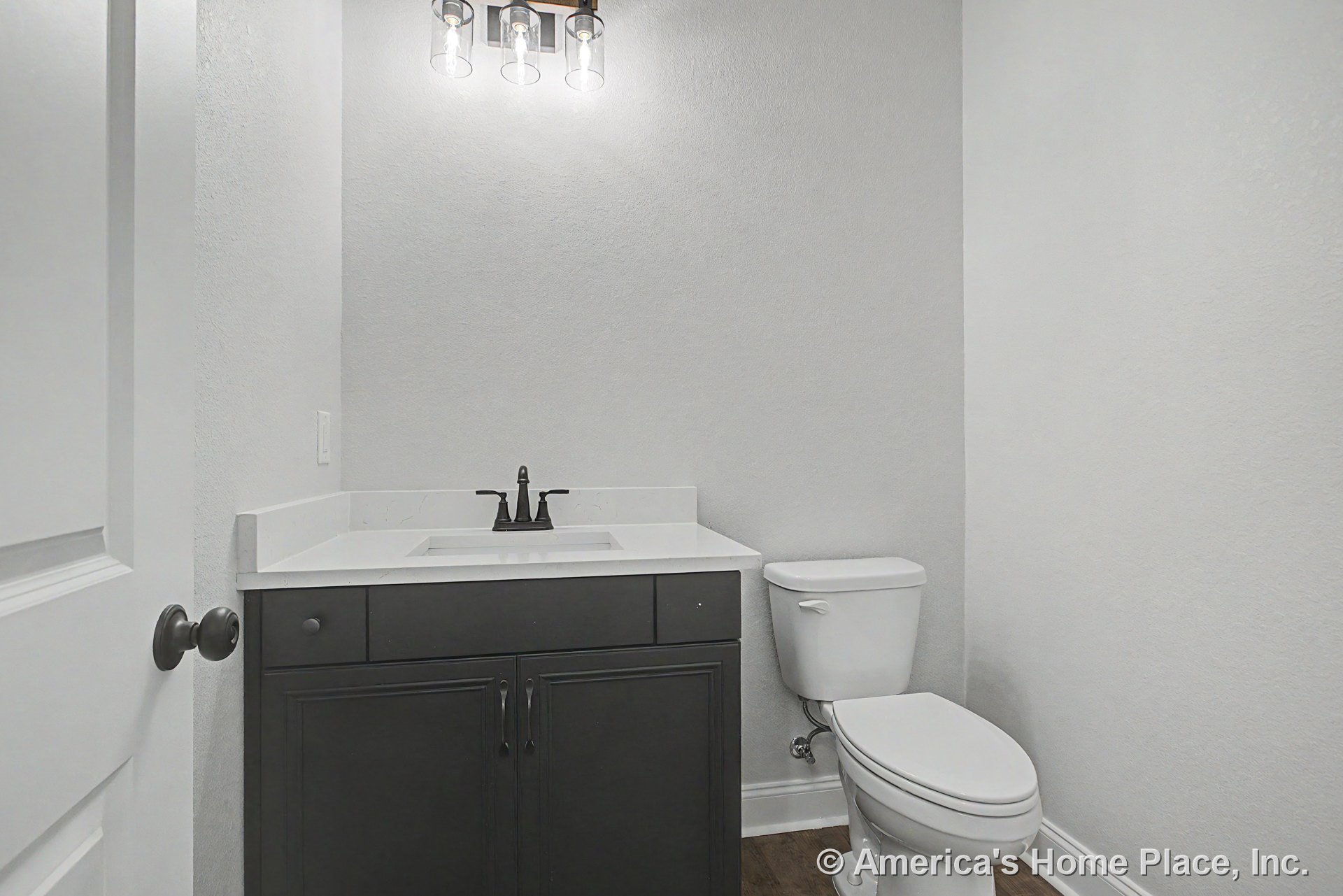 Dark wood vanity with white quartz countertop, rectangular undermount sink, modern three-bulb wall sconce, white toilet, and wood-look flooring.