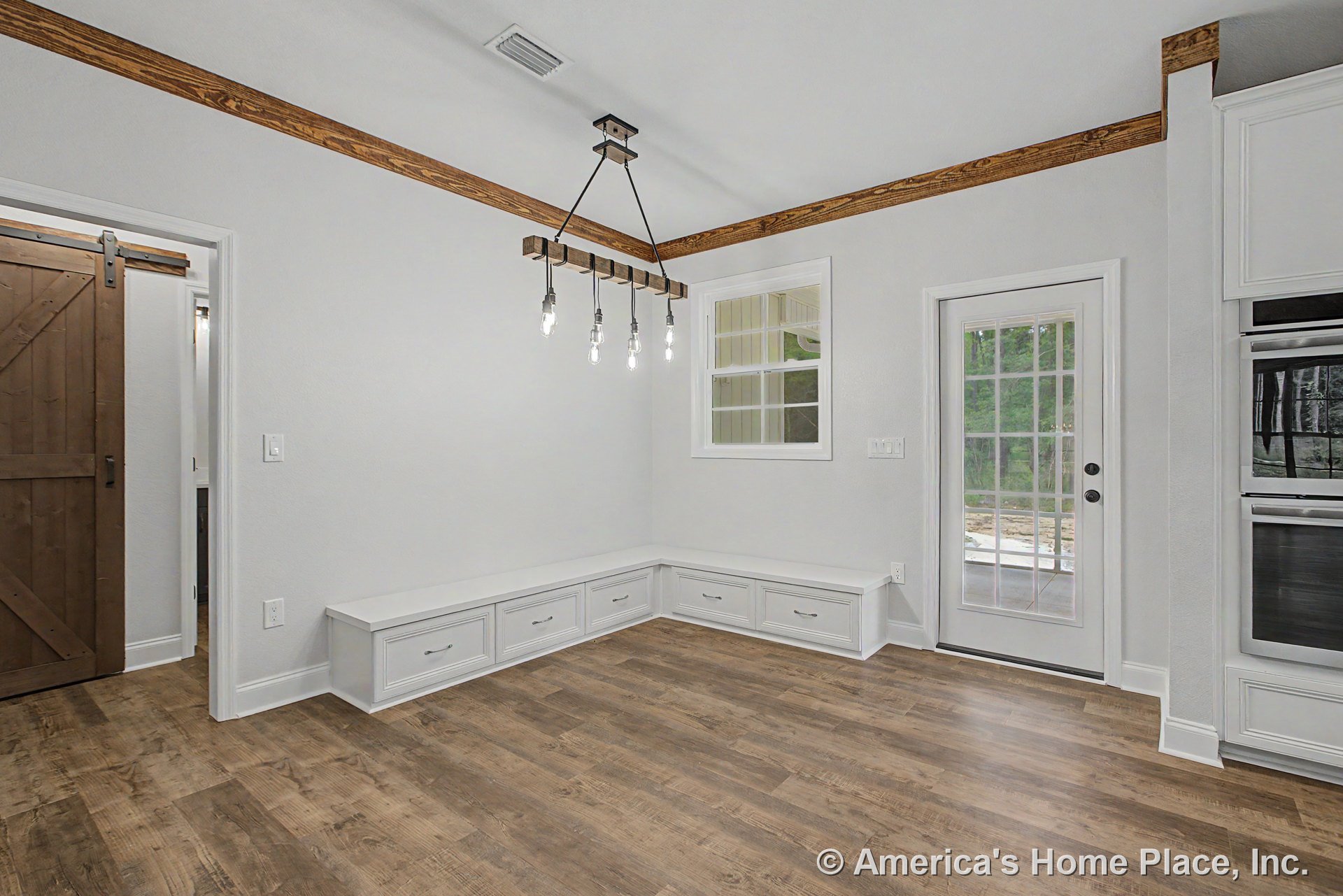 Built-in white bench cabinetry with storage drawers lines the dining area, complemented by wood-look flooring, rustic wood beam ceiling trim, a glass door to the exterior, and a