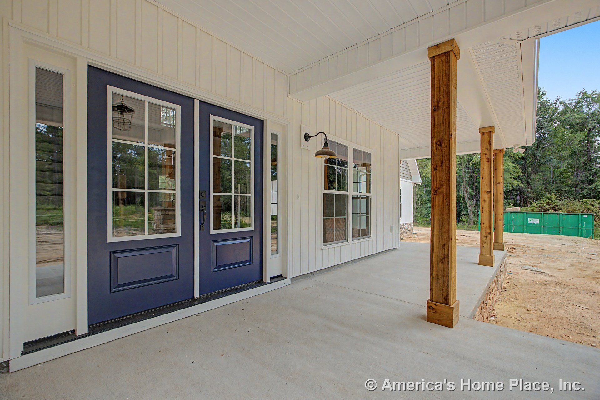 Covered front porch with wooden support columns, double glass entry doors, vertical board and batten siding, exterior wall-mounted light fixture, concrete flooring, and finished