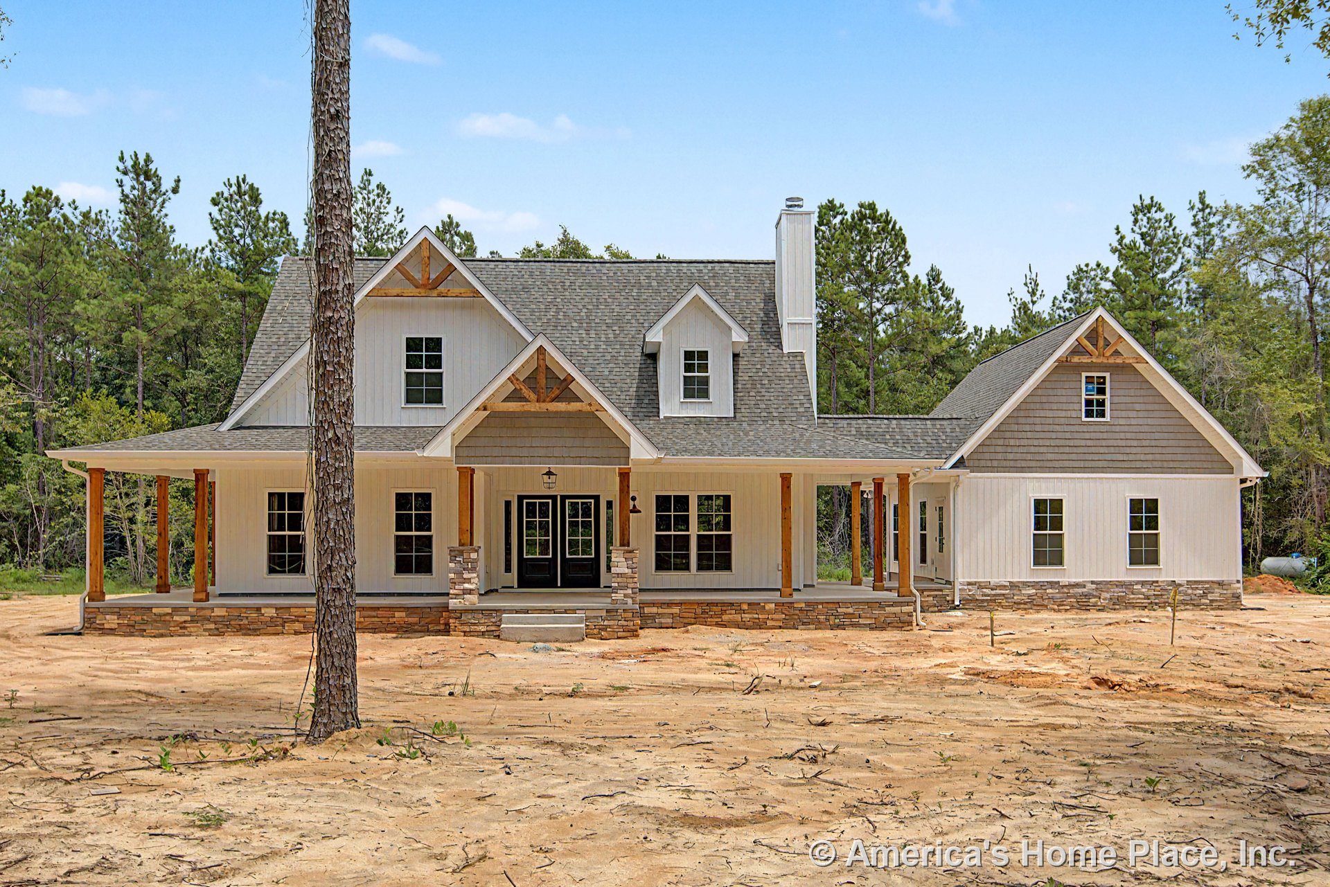 Large covered front porch with stone pillar bases, board-and-batten siding, multiple gabled rooflines, double glass-panel front doors, and exposed wood porch posts.