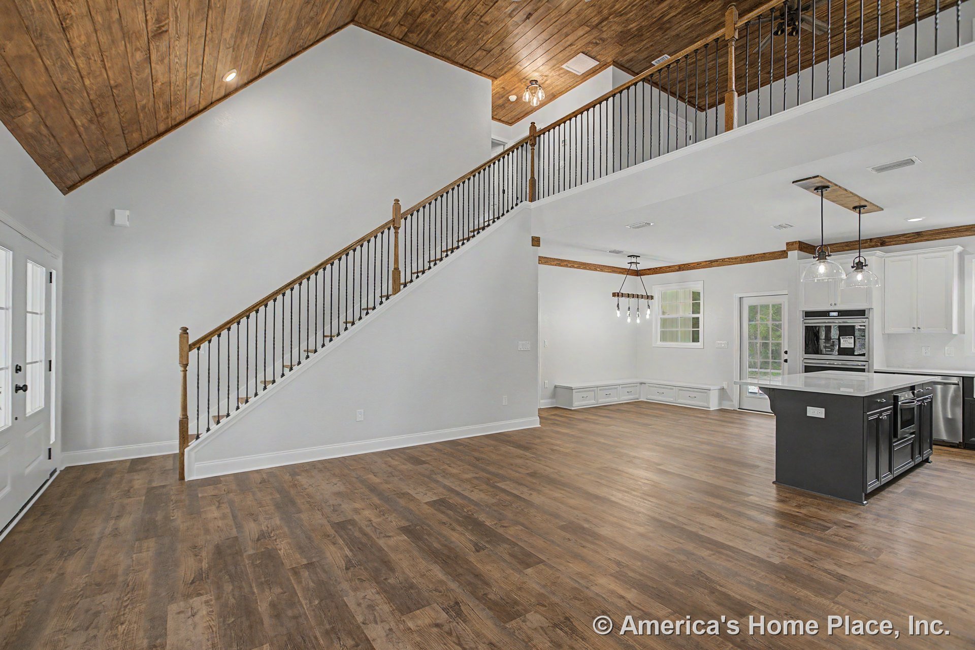Open concept living area with wood plank flooring, vaulted wood ceiling, iron baluster staircase, kitchen island with white cabinetry and double ovens, built-in bench cabinetry