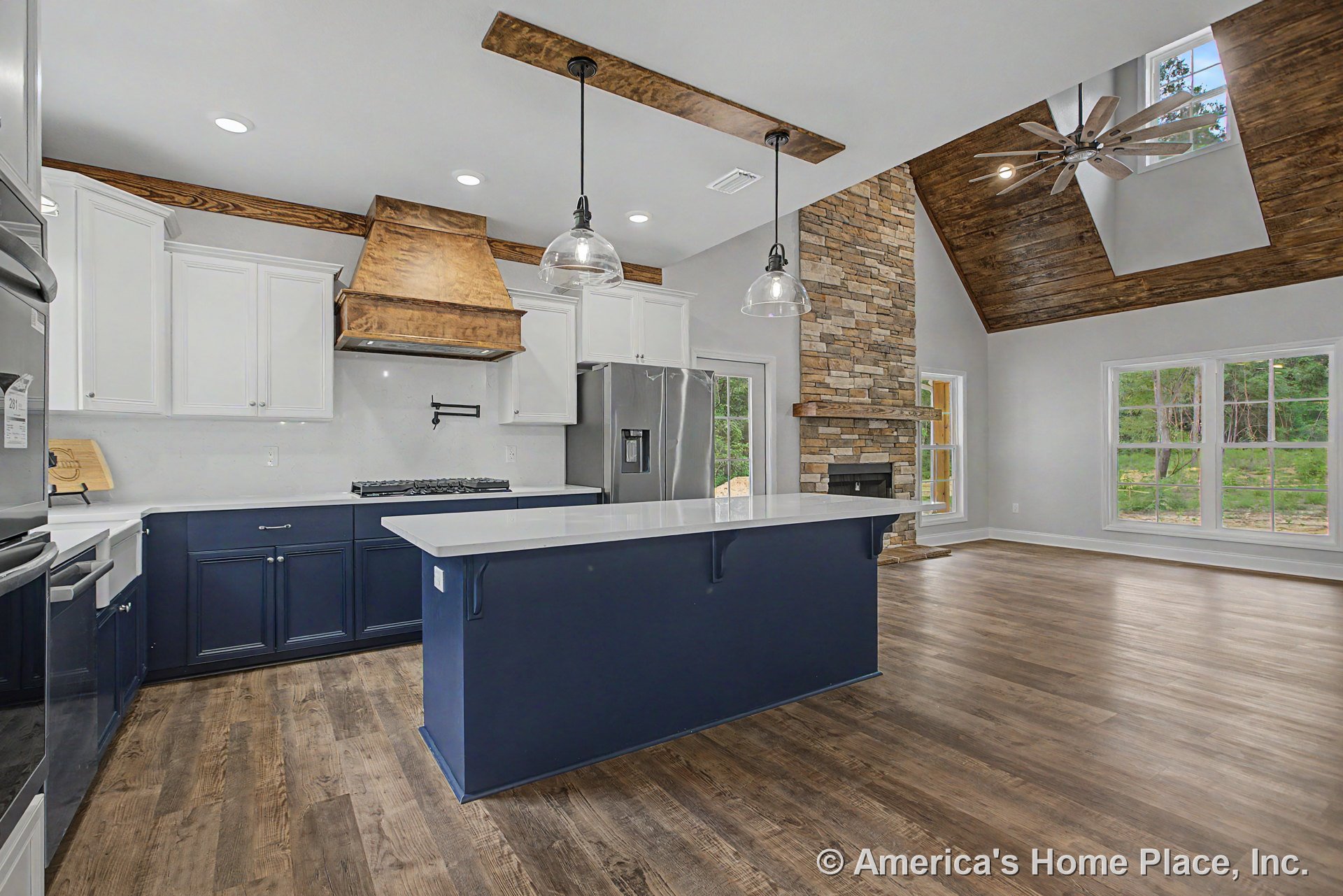 Navy kitchen island with quartz countertops and pendant lighting, white upper cabinetry, wood range hood with pot filler, stainless appliances, open concept layout leading to