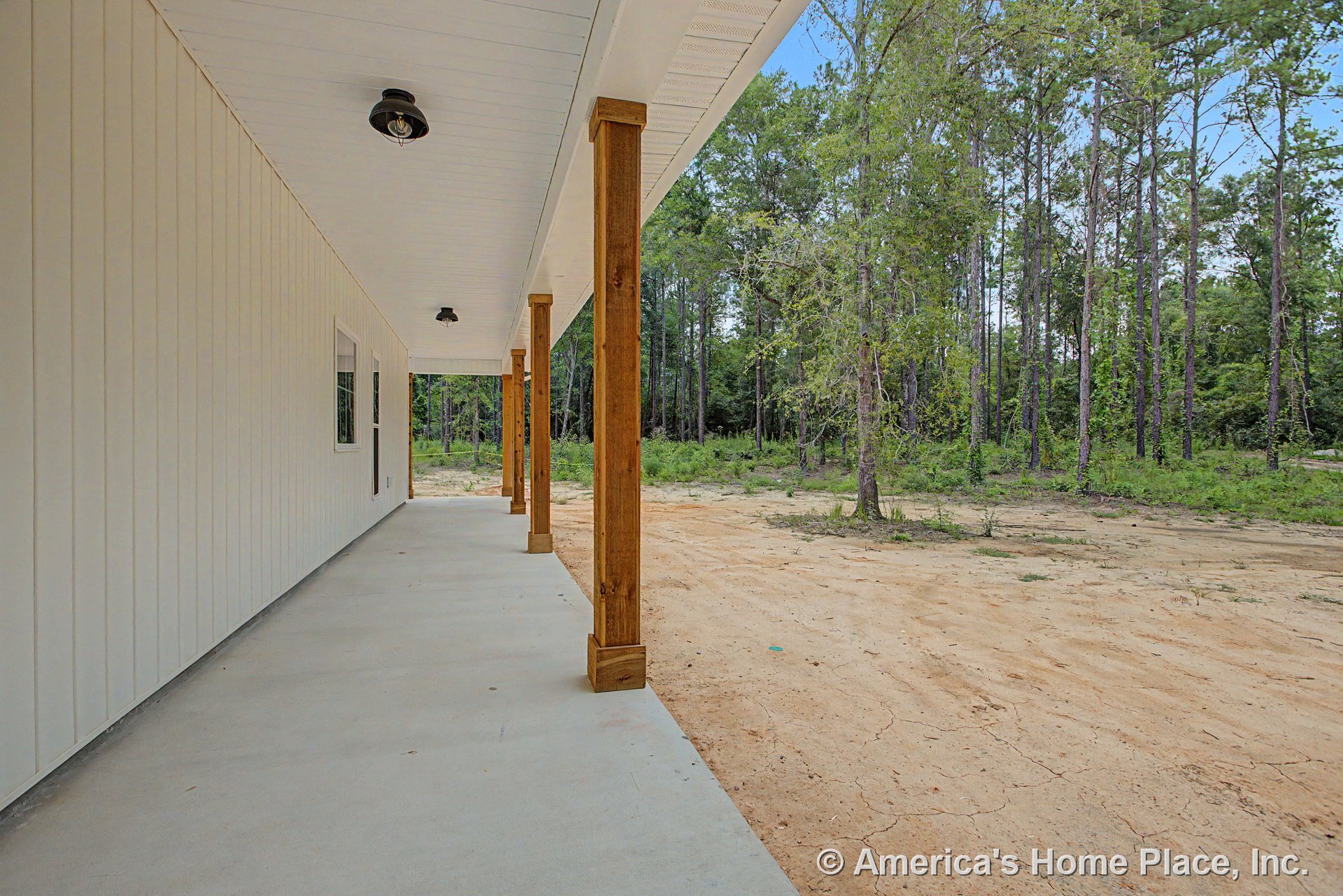 Covered concrete front porch with wood support columns, vertical exterior siding, white beadboard ceiling with built-in lights, and single window on porch wall.