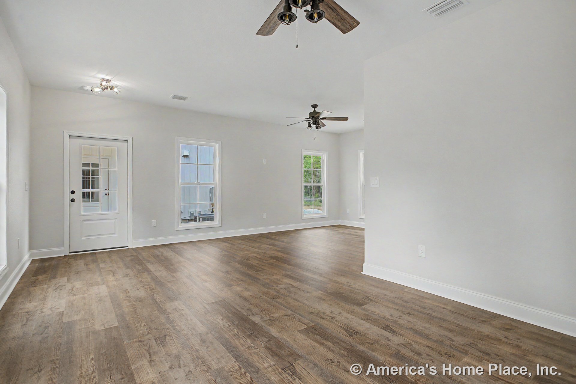 Wood-look plank flooring with white trim and baseboards, double ceiling fans, large windows, glass panel exterior door, neutral wall color, open layout with abundant natural light.