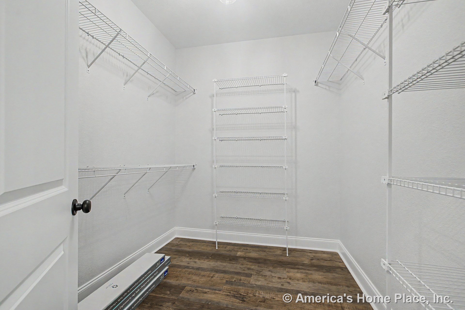 Walk-in closet with multiple white wire shelving units, wood-look flooring, white trim, painted walls, and overhead ceiling light.