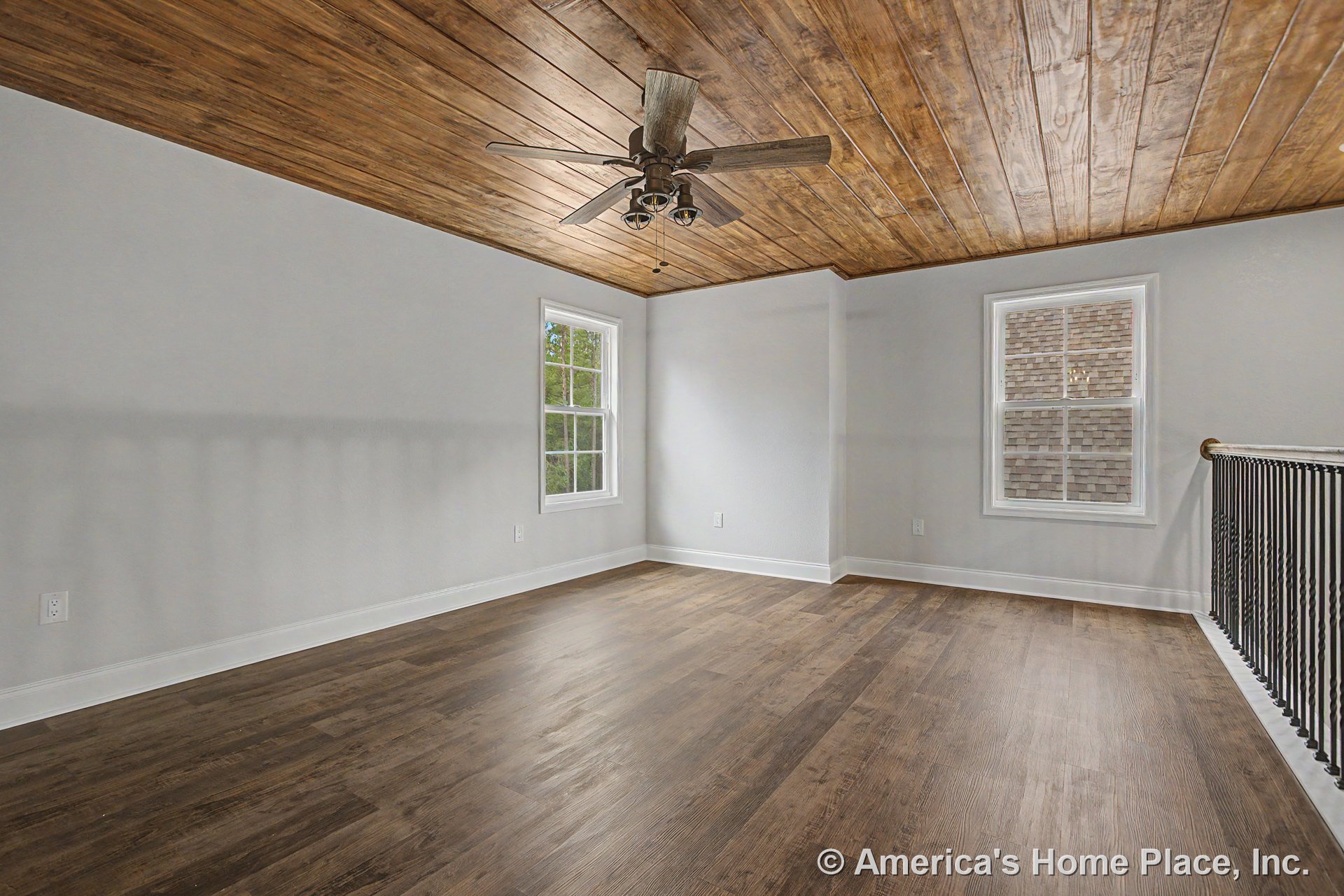 Upstairs room with wood plank ceiling, ceiling fan with lights, matching wood-look flooring, two double-hung windows, white baseboards, metal stair railing, and neutral walls.