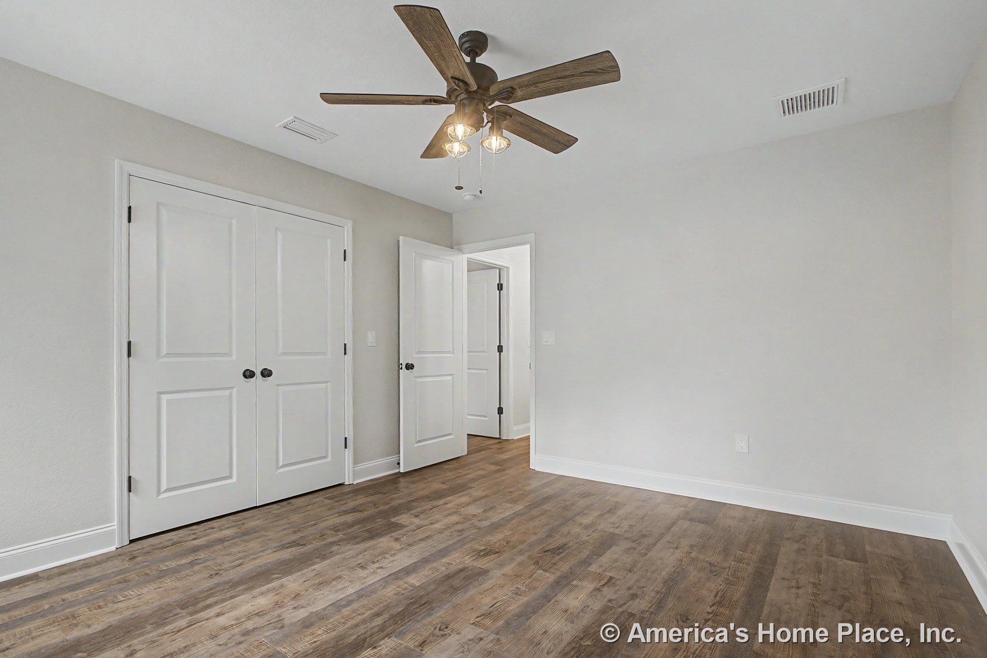 Bedroom with wood-look plank flooring, double white closet doors, ceiling fan with integrated lighting, white trim and baseboards, neutral wall color, standard interior door, vent