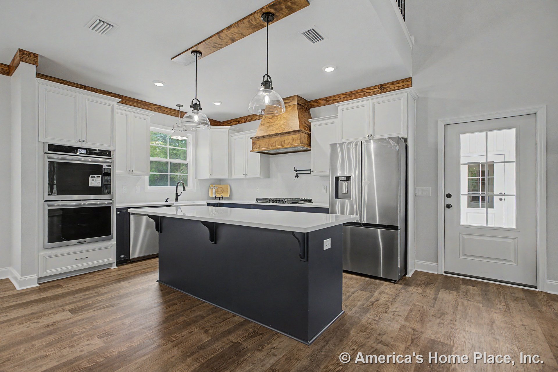 White shaker cabinets and wood trim frame a spacious kitchen with a large quartz island, stainless steel double wall oven and refrigerator, wood-look flooring, pendant lights above