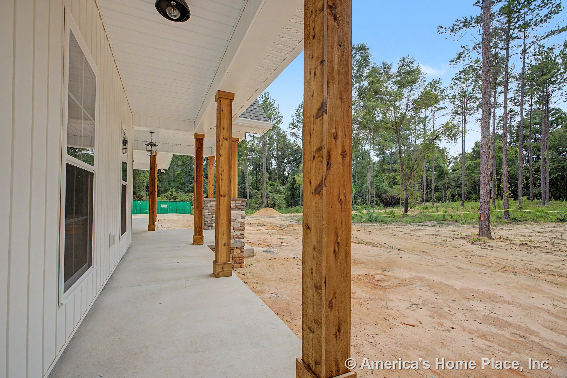 Covered front porch with white vertical siding, large windows, wood support columns with stone base accents, concrete flooring, outdoor ceiling lights, and detailed trim.