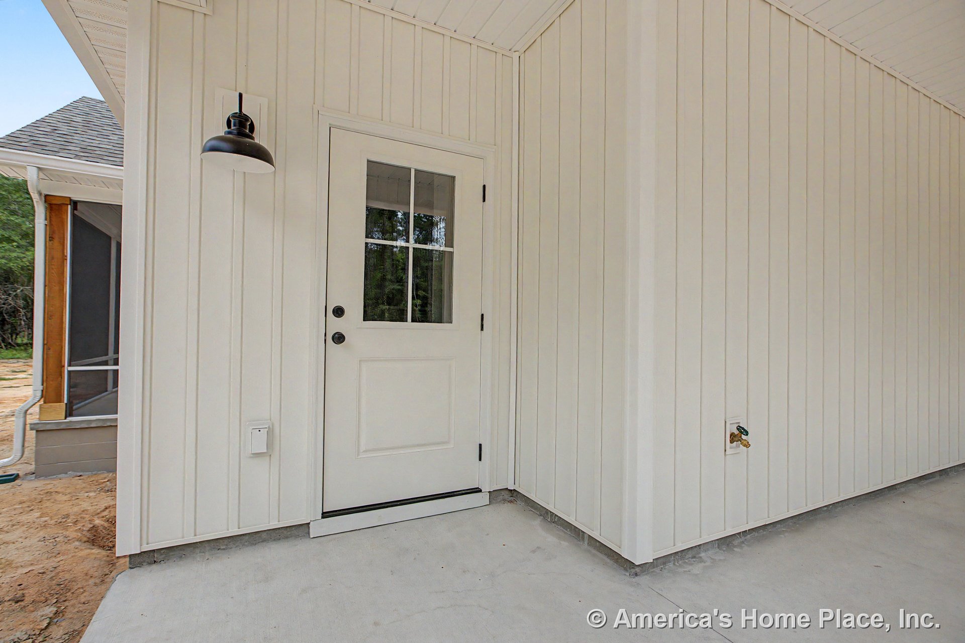 Covered exterior entry with vertical board and batten siding, white paneled door featuring divided glass, wall-mounted black outdoor light fixture, concrete porch floor, beadboard