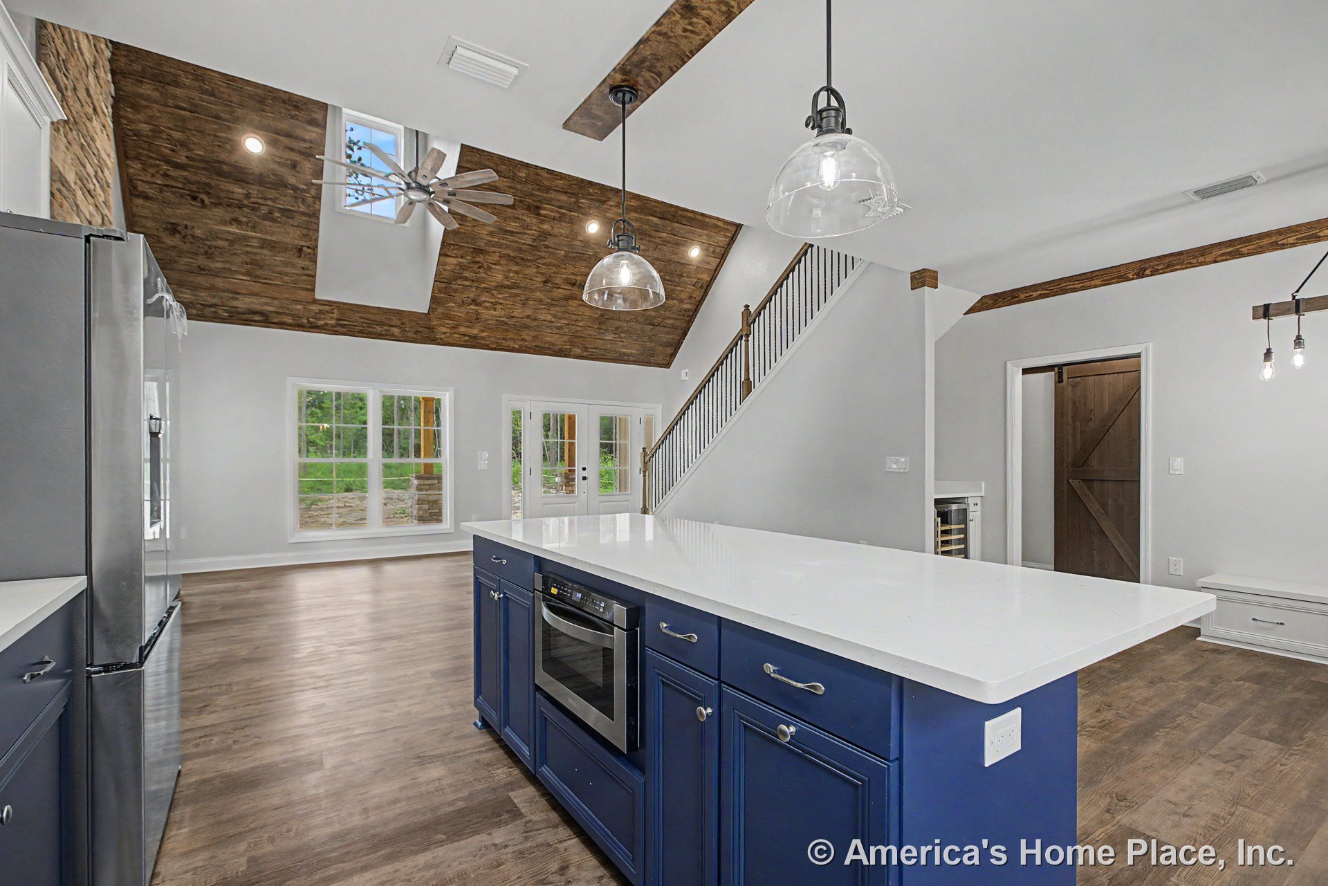 Spacious kitchen with vaulted wood ceiling and exposed beams, large island featuring blue cabinetry and quartz countertops, pendant lighting above, stainless steel appliances, wide