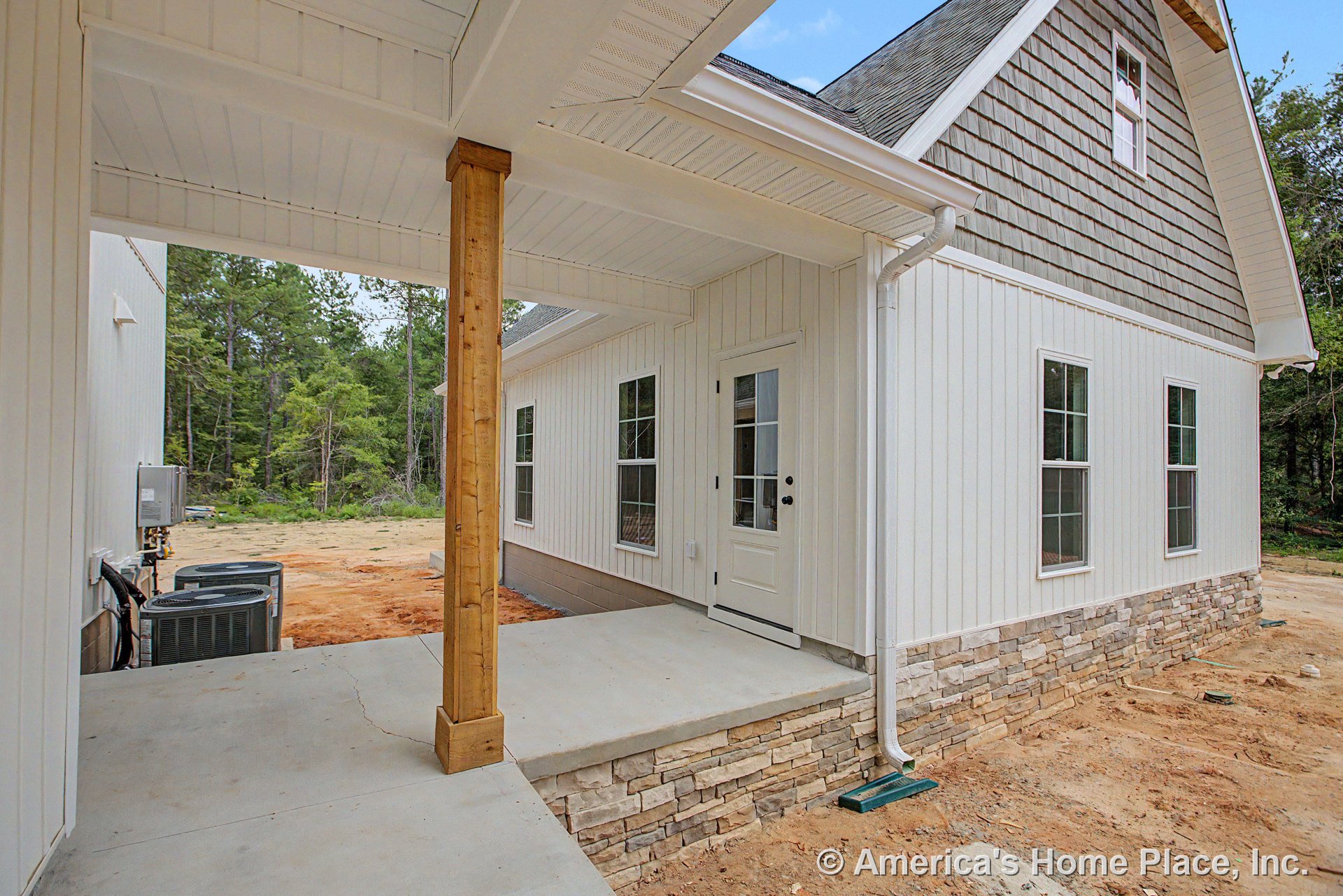 Vertical white siding and stone veneer foundation, covered porch with wood column, multiple double-hung windows, white exterior door with glass panels, vented soffit ceiling