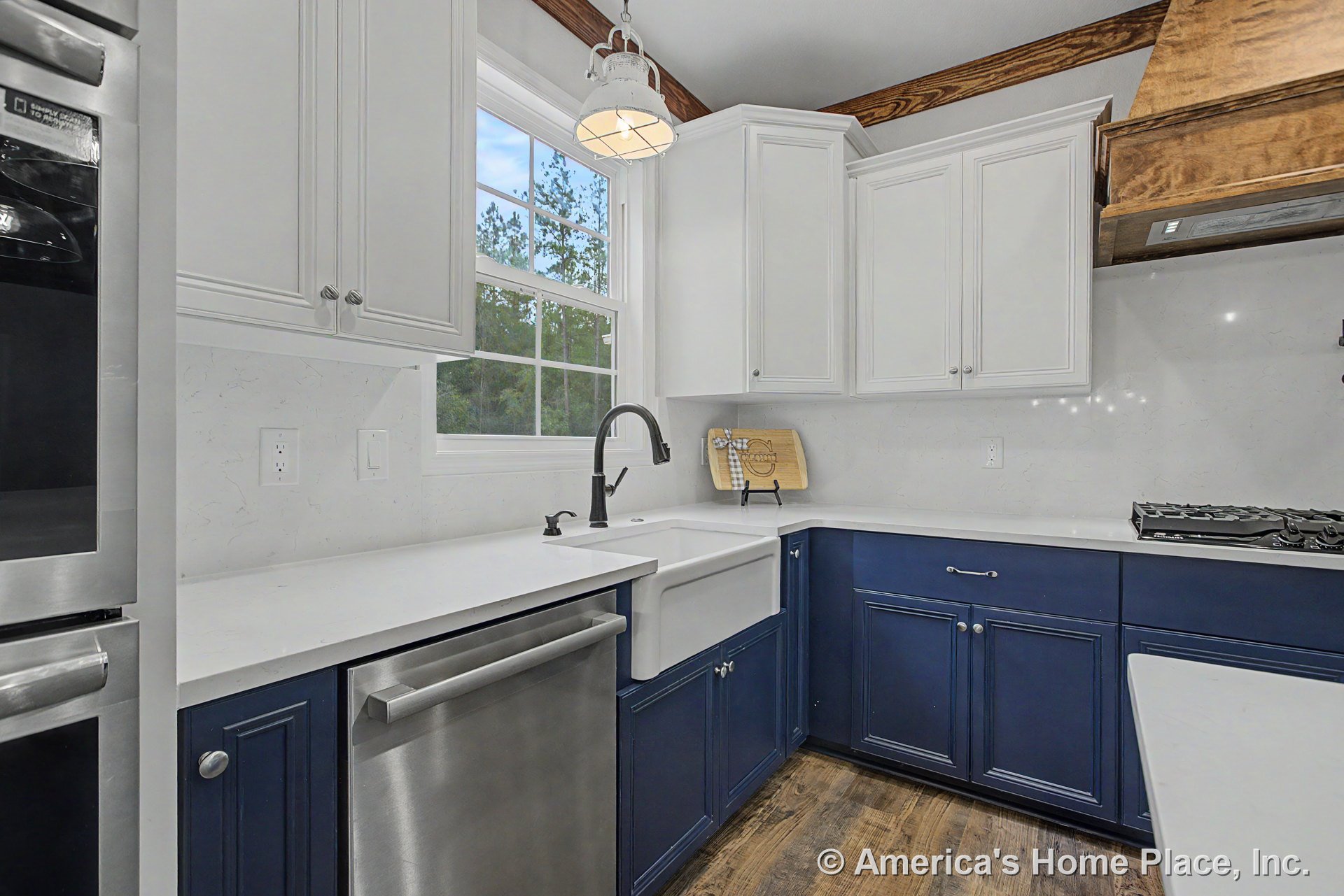 Farmhouse sink beneath a window, white upper cabinets, blue lower cabinets, quartz countertops, wood vent hood above gas cooktop, pendant light fixture, stainless dishwasher, wood