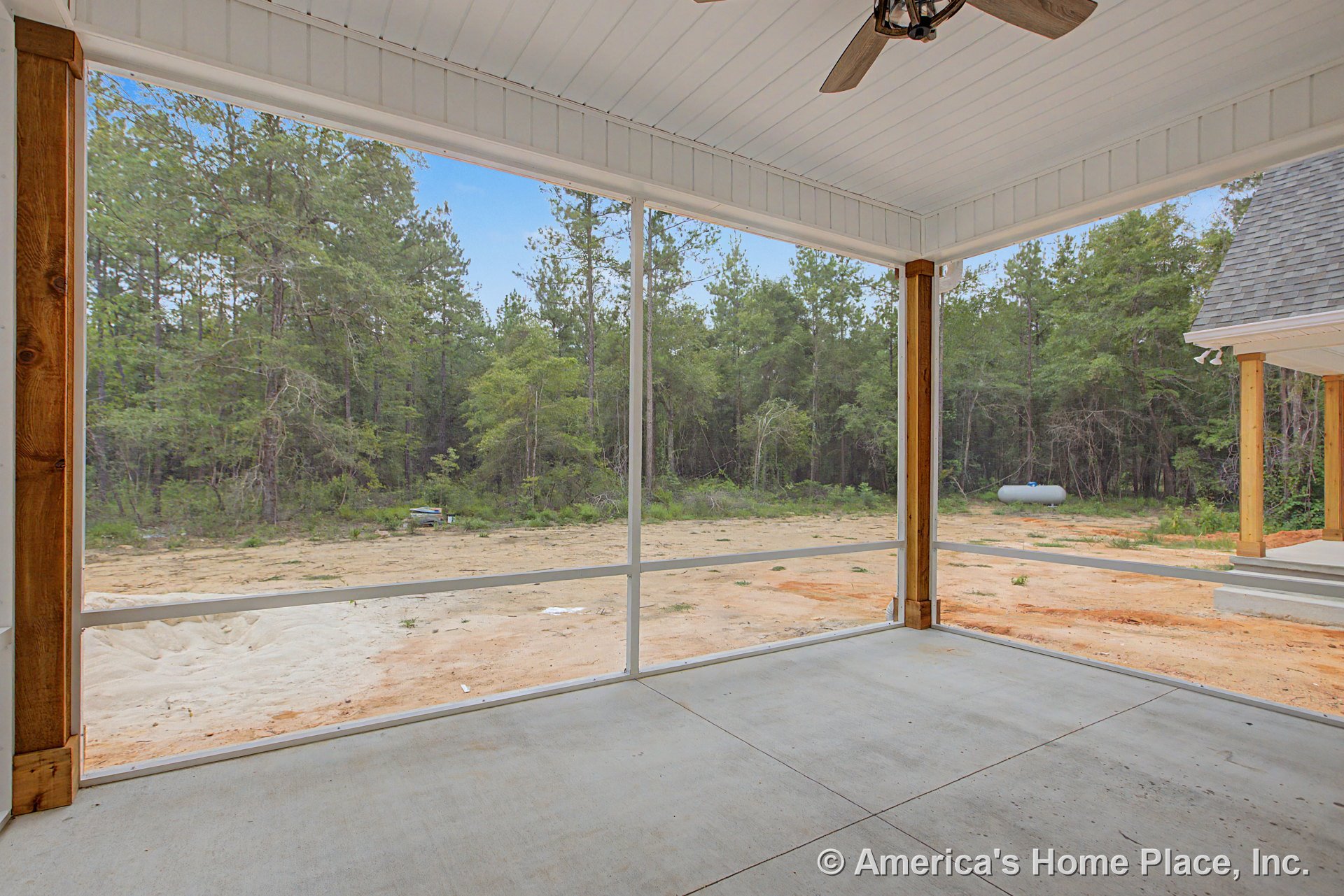 Screened-in porch with concrete flooring, wood support posts, white paneled ceiling, ceiling fan fixture, exterior steps, and forest backdrop.