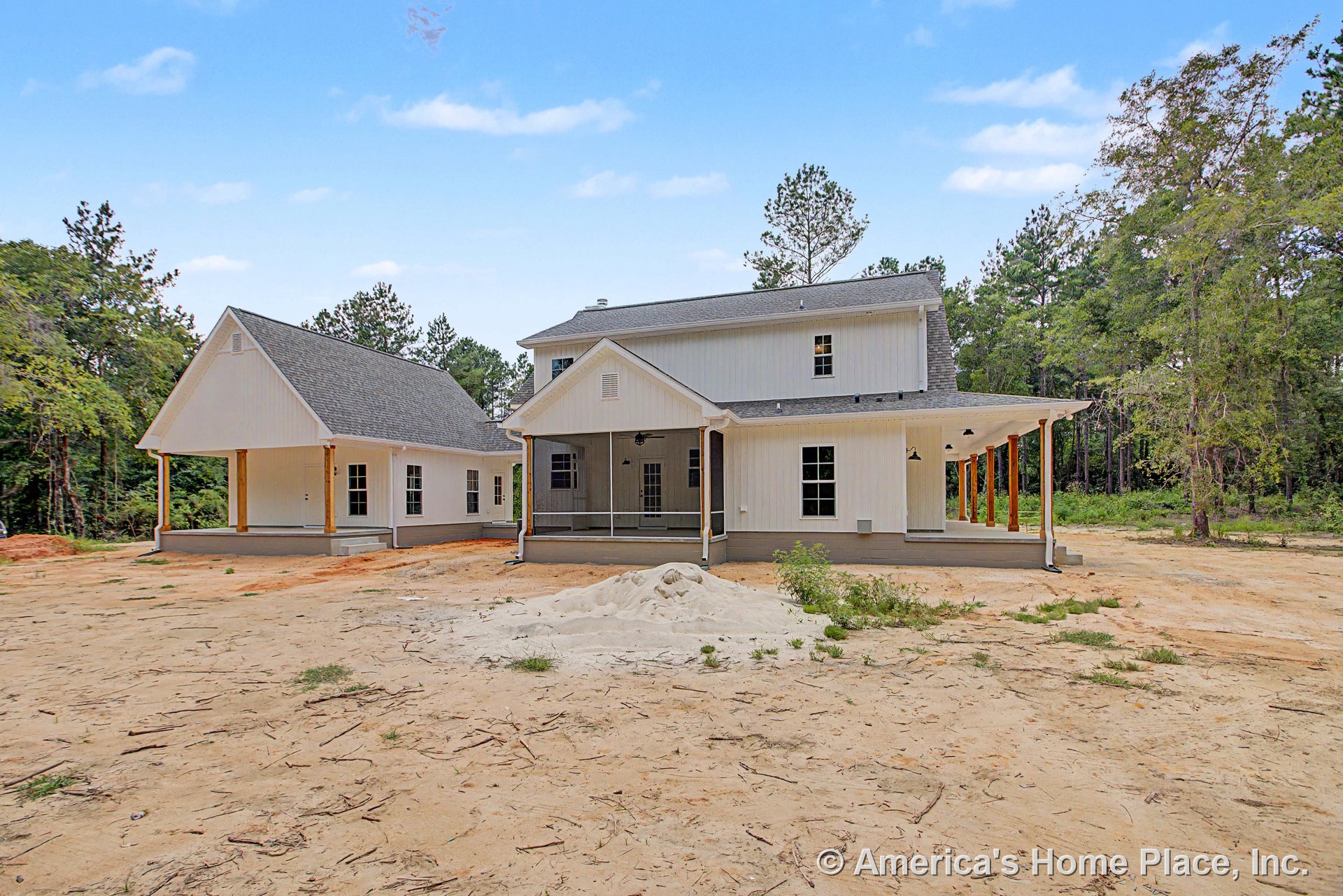 Board and batten siding with prominent wood columns supporting a covered wraparound porch, multiple double-hung windows, gable roof design, outdoor lighting fixtures, and detailed