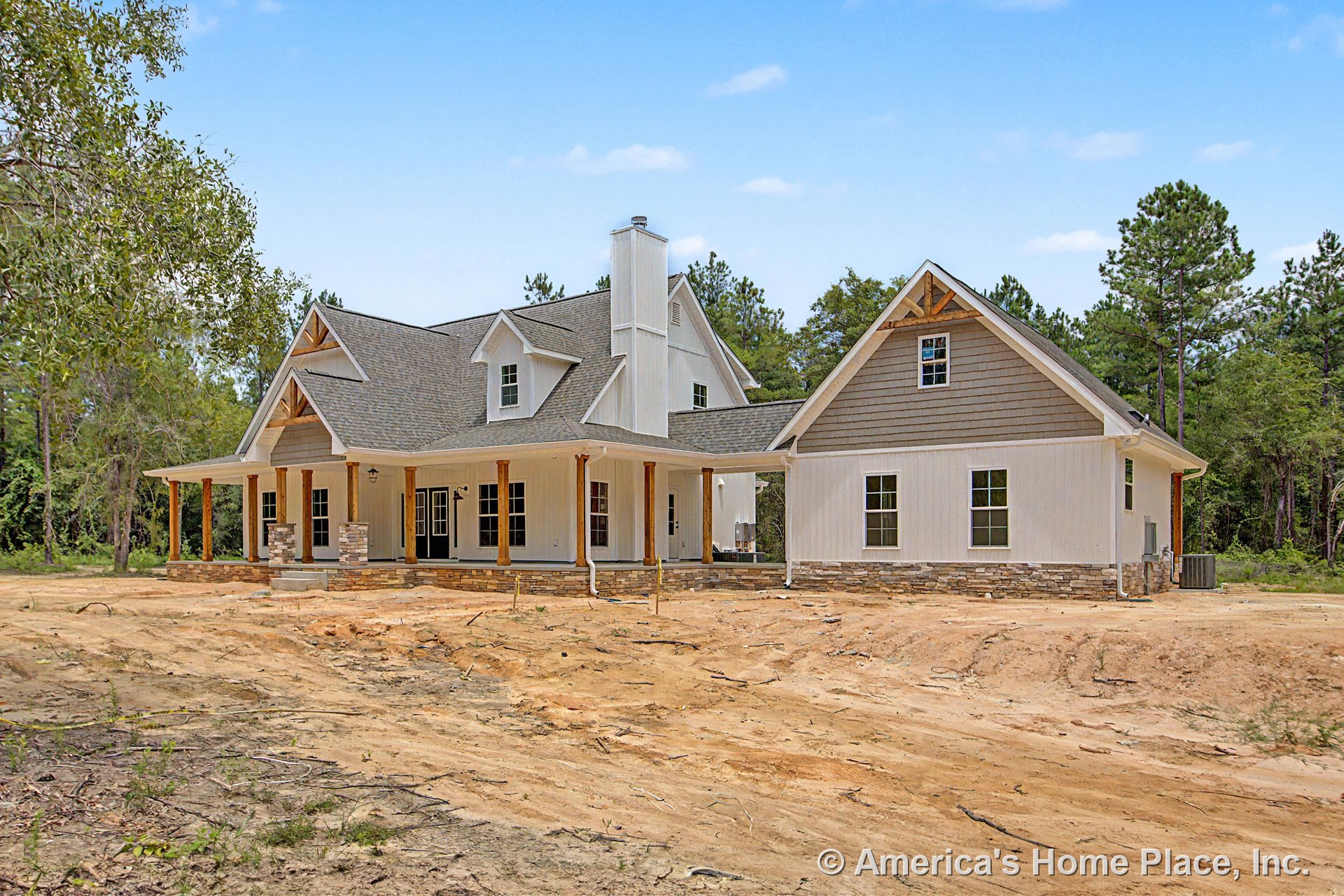 Large covered front porch with stone column bases, board-and-batten siding, multiple gabled rooflines, exterior chimney, trimmed windows, wood posts, shingle roof, and prominent