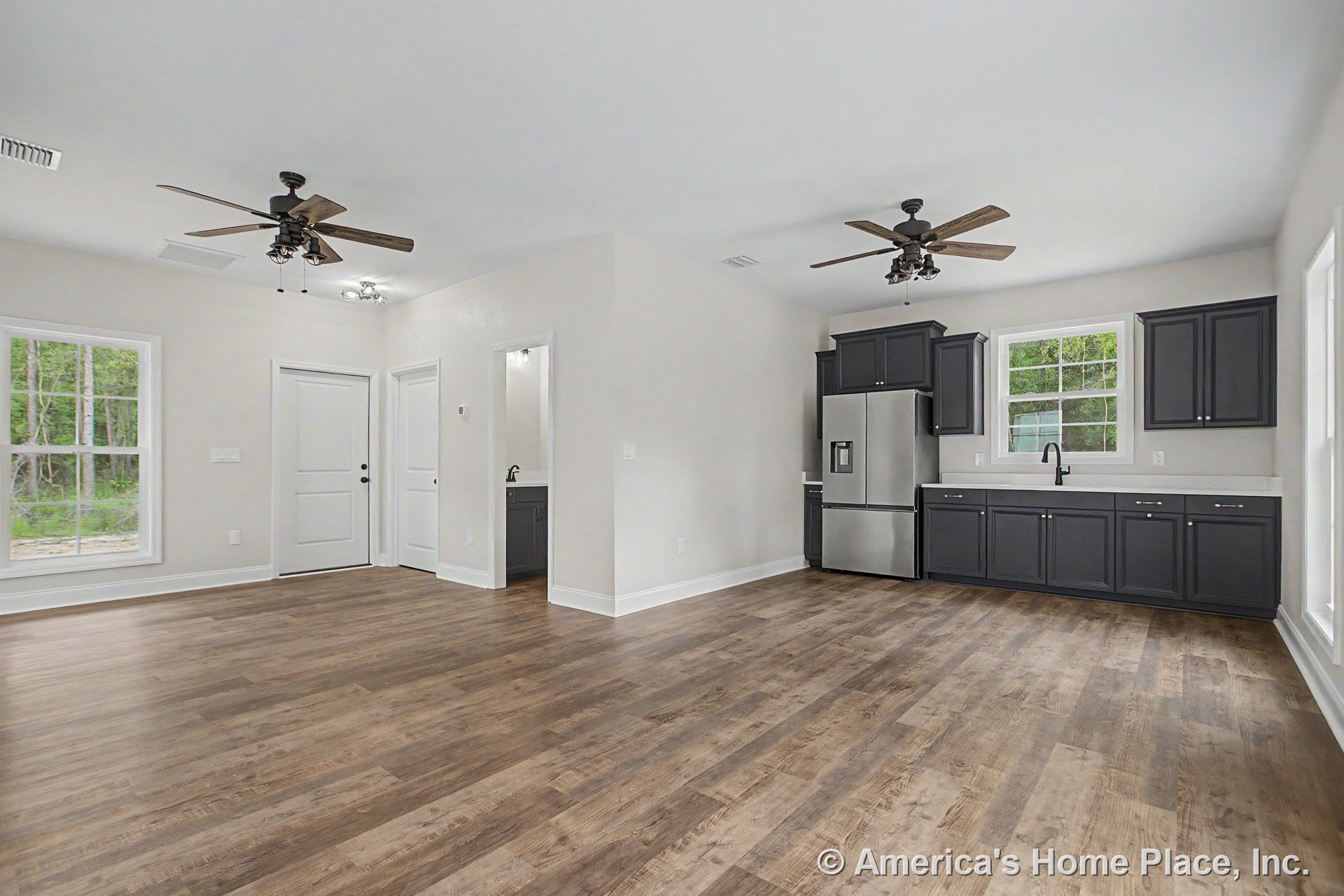 Open kitchen and living area with dark cabinetry, stainless steel refrigerator, white quartz countertops, wood-look plank flooring, large windows, ceiling fans with lights