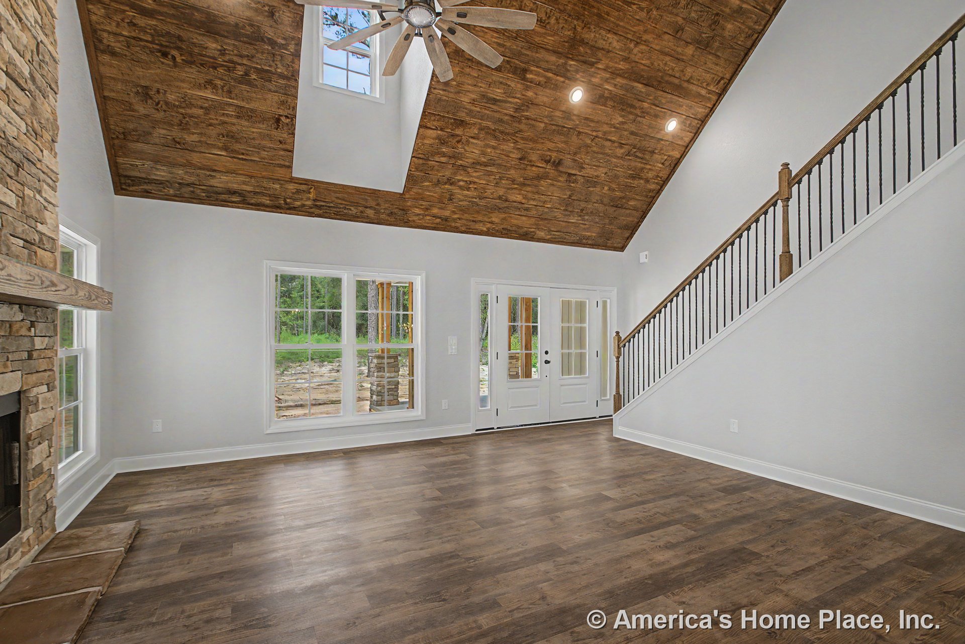 Vaulted wood ceiling with recessed lighting and ceiling fan, stone fireplace centered between large windows with white trim, wood-look flooring, staircase with iron balusters, and