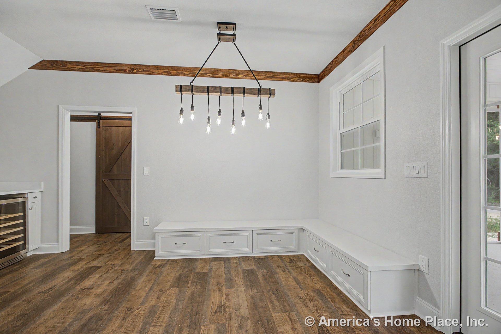 Built-in white bench cabinetry with storage drawers lines the dining nook, complemented by wood-look plank flooring, modern pendant lighting, white window trim and casing, a