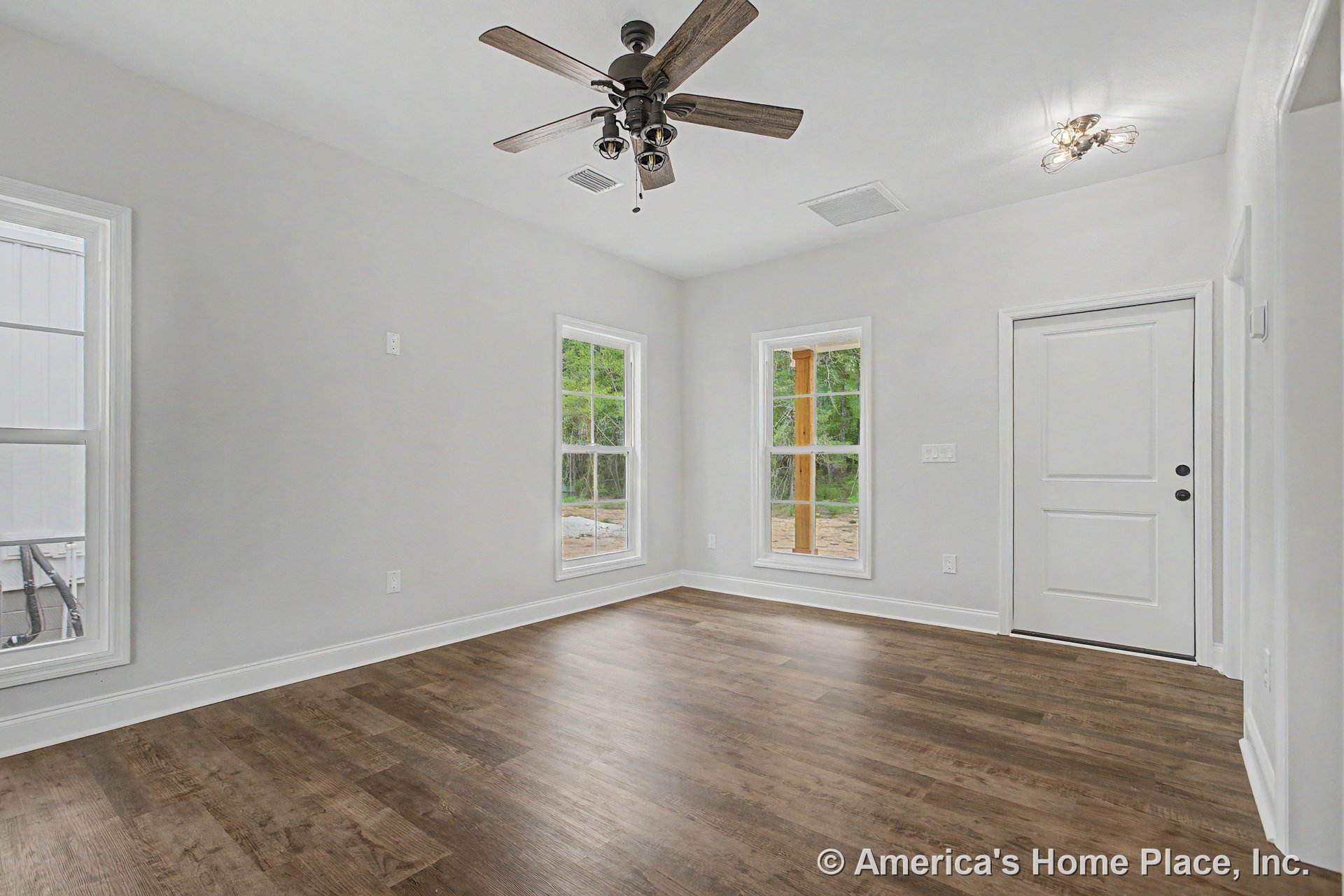 Wood-look plank flooring, white trim and baseboards, two large windows allowing natural light, ceiling fan with built-in lights, flush mount ceiling light, white paneled door, and