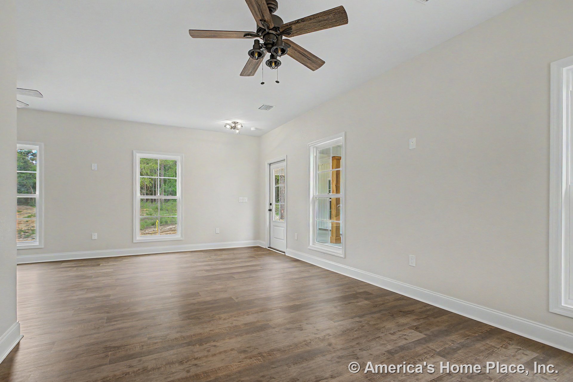 Living room with wood-look plank flooring, white trim and baseboards, neutral wall color, multiple double-hung windows, ceiling fan with integrated light fixture, and exterior door