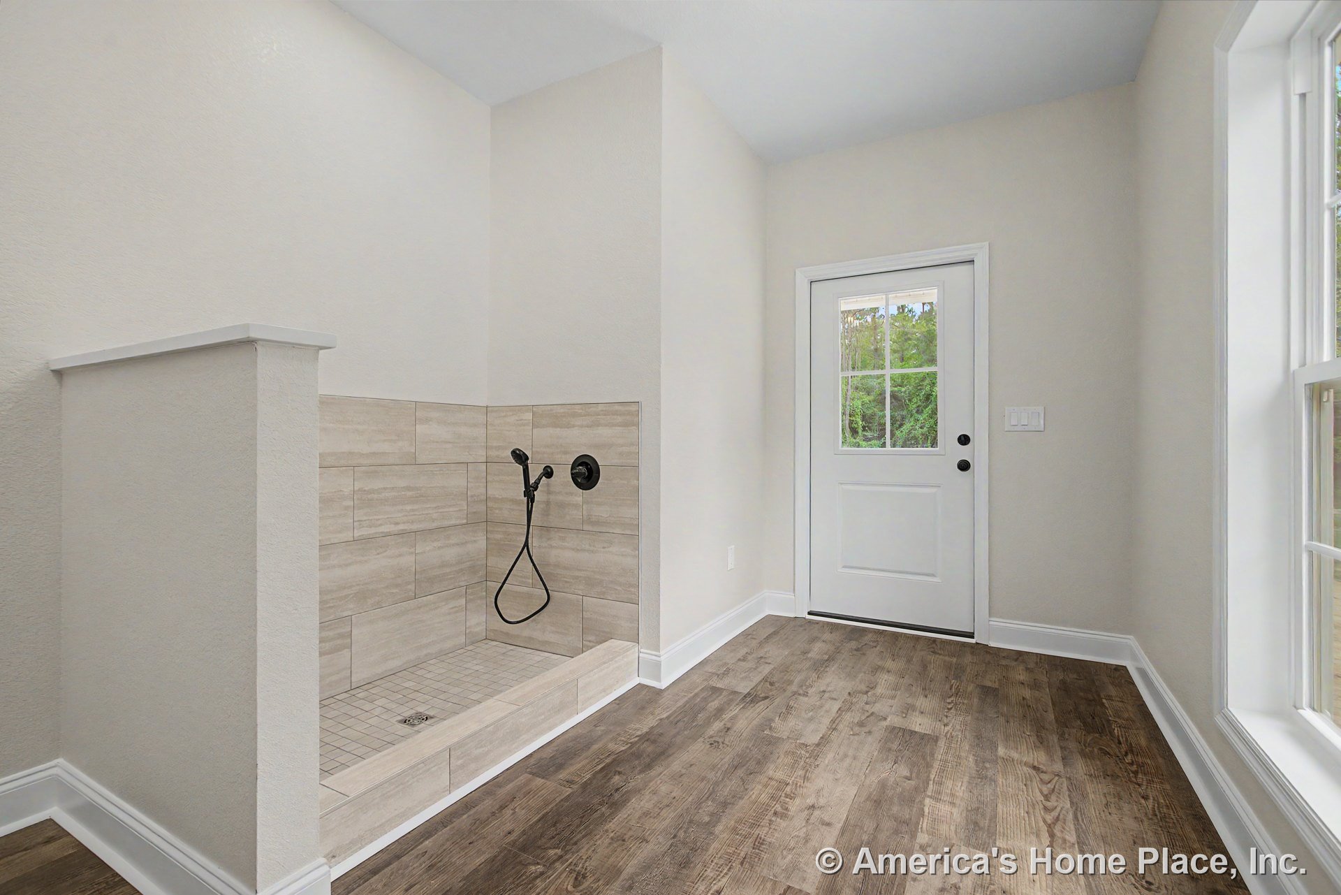 Mudroom with built-in tiled pet shower, handheld sprayer, wood-look plank flooring, white trim and baseboards, exterior door with window, and large window providing natural light.