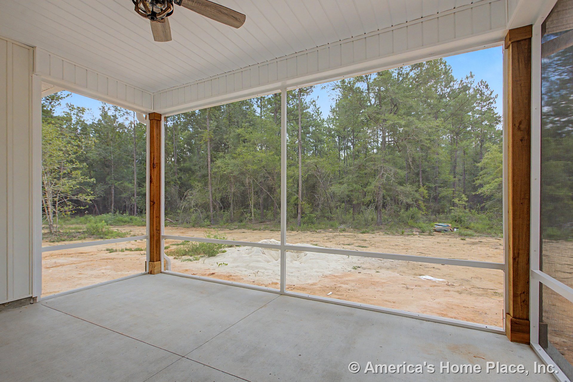 Screened porch with concrete flooring, wood trim posts, white paneled ceiling, built-in ceiling fan, and forest view through mesh enclosure.