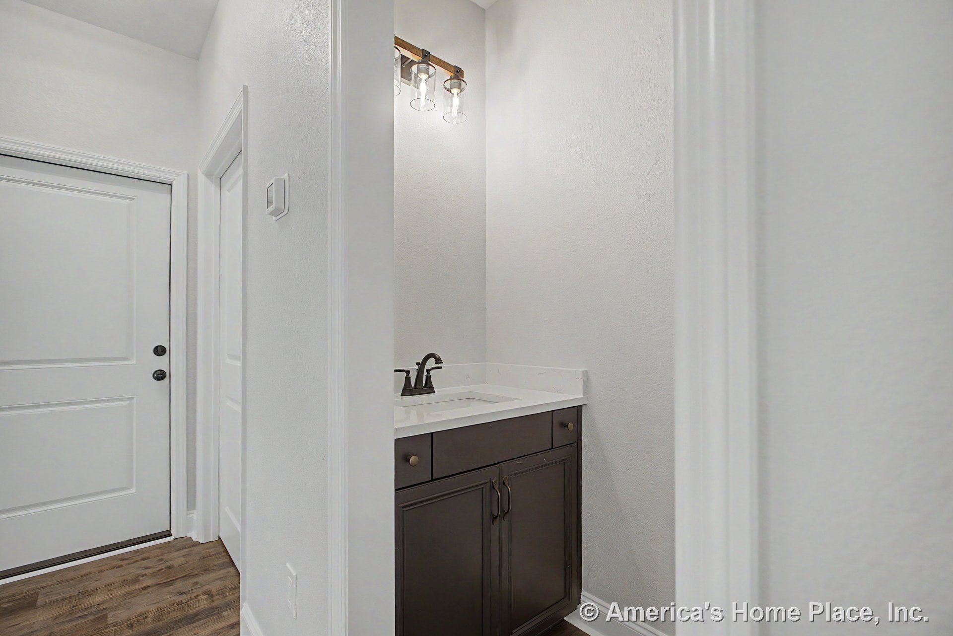 Small bathroom with dark wood vanity, white countertop, matte black faucet, three-light modern fixture, white trim, wood-look flooring, and white sink.