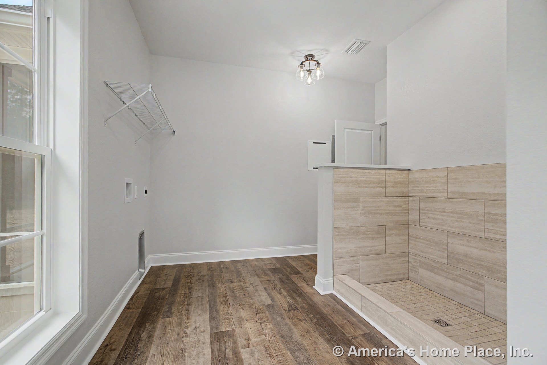 Laundry room with built-in tiled pet shower, wood-look plank flooring, white trim and baseboards, large divided-light window, wire wall-mounted shelf, ceiling light fixture, and