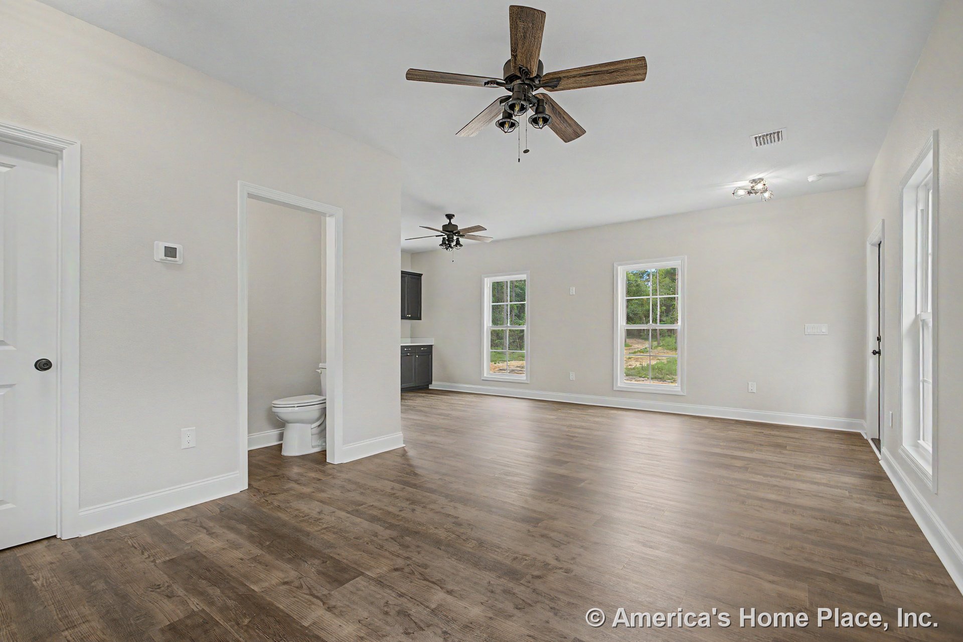 Open living area with wood-look plank flooring, double ceiling fans with integrated lighting, large double-hung windows, white trim and baseboards, recessed lighting, adjacent