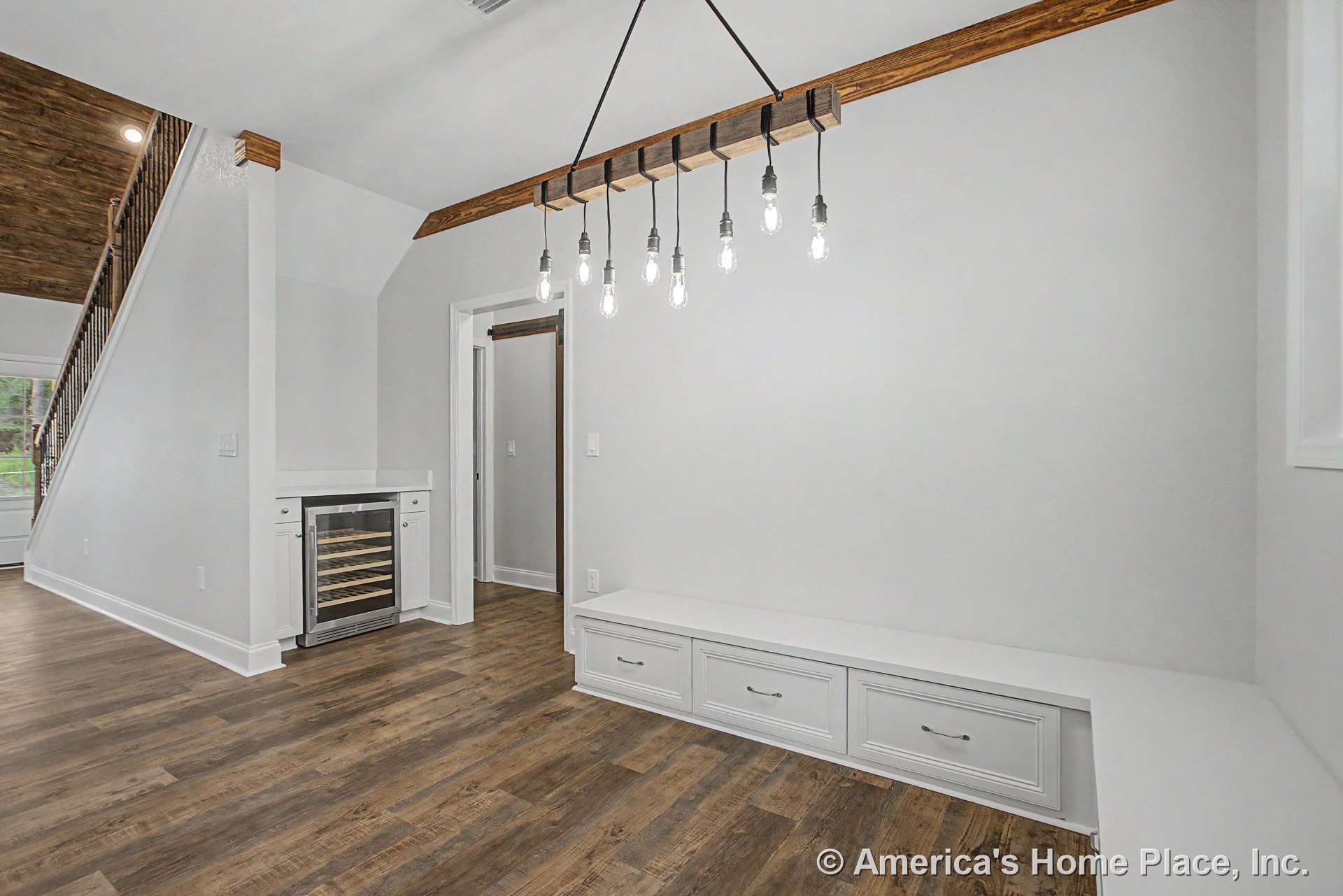 Built-in bench with storage drawers beside under-counter wine cooler, wood-look plank flooring, exposed wood ceiling beam, modern pendant light fixture, white trim and baseboards
