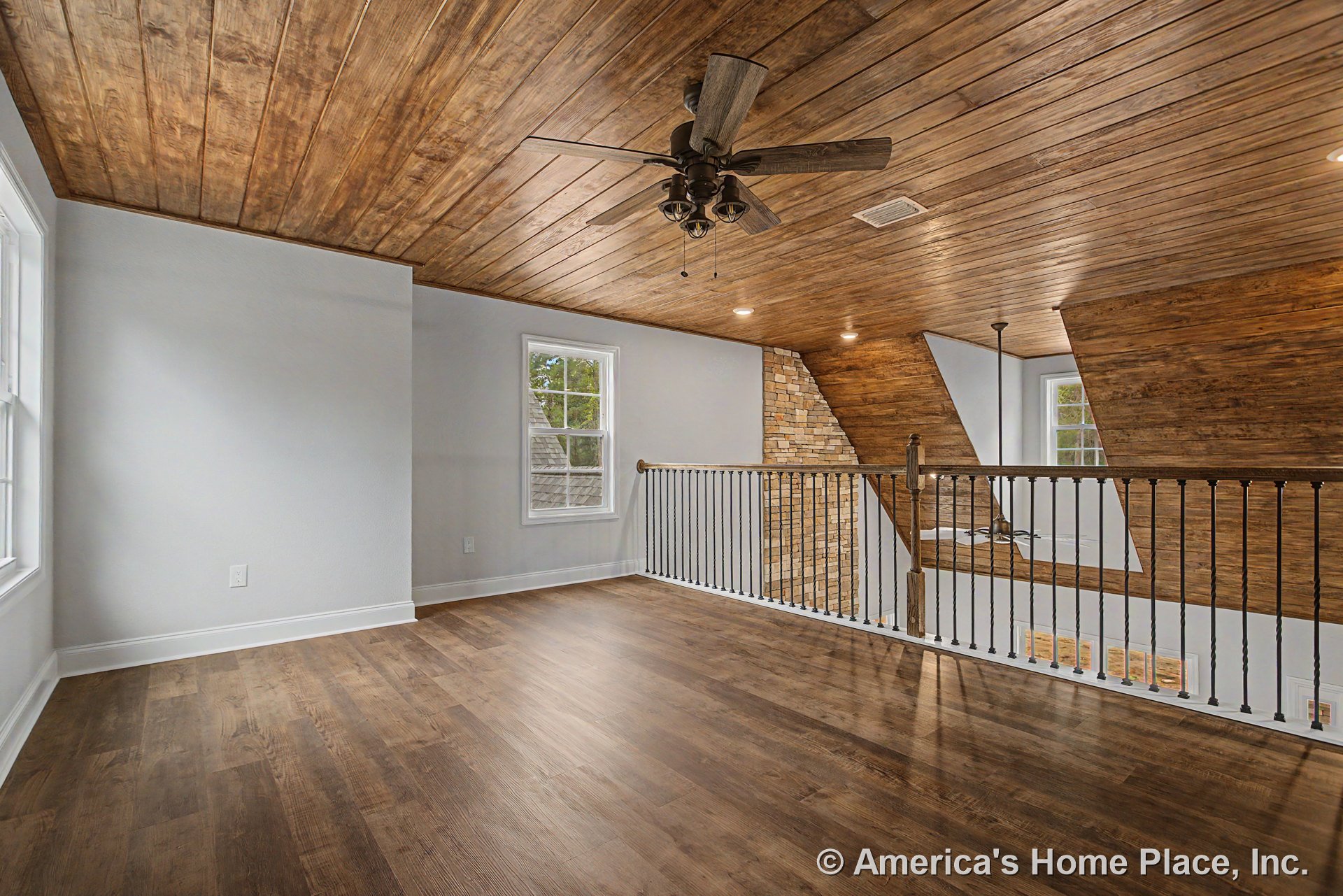 Loft with wood plank ceiling, recessed lighting, ceiling fan, matching wood flooring, wrought iron open railing, stone accent wall, and large windows with trim.