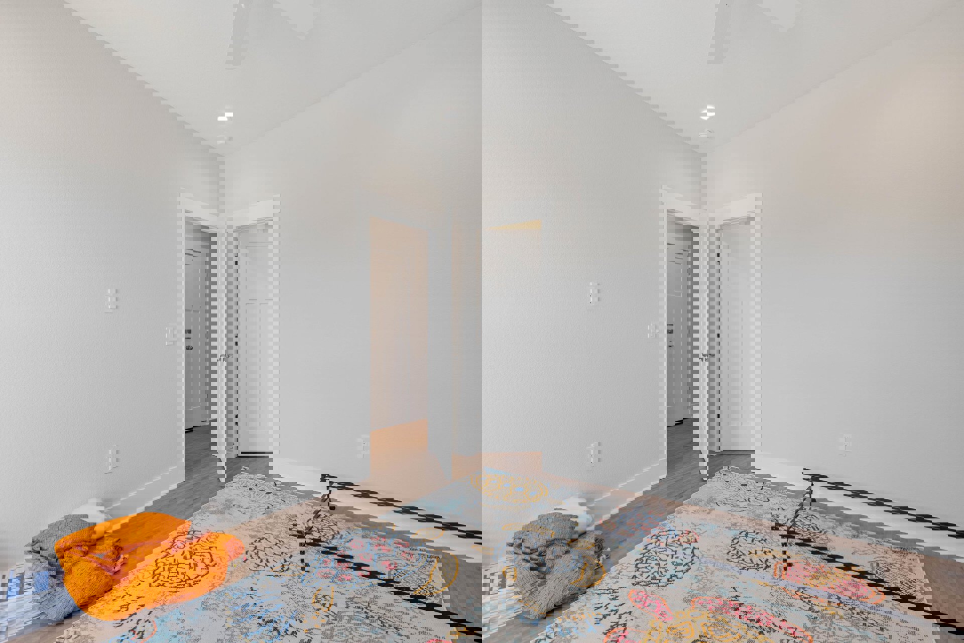 Bedroom with white walls, laminate flooring, turtle-patterned rug, ceiling fan, and bed topped with an orange blanket