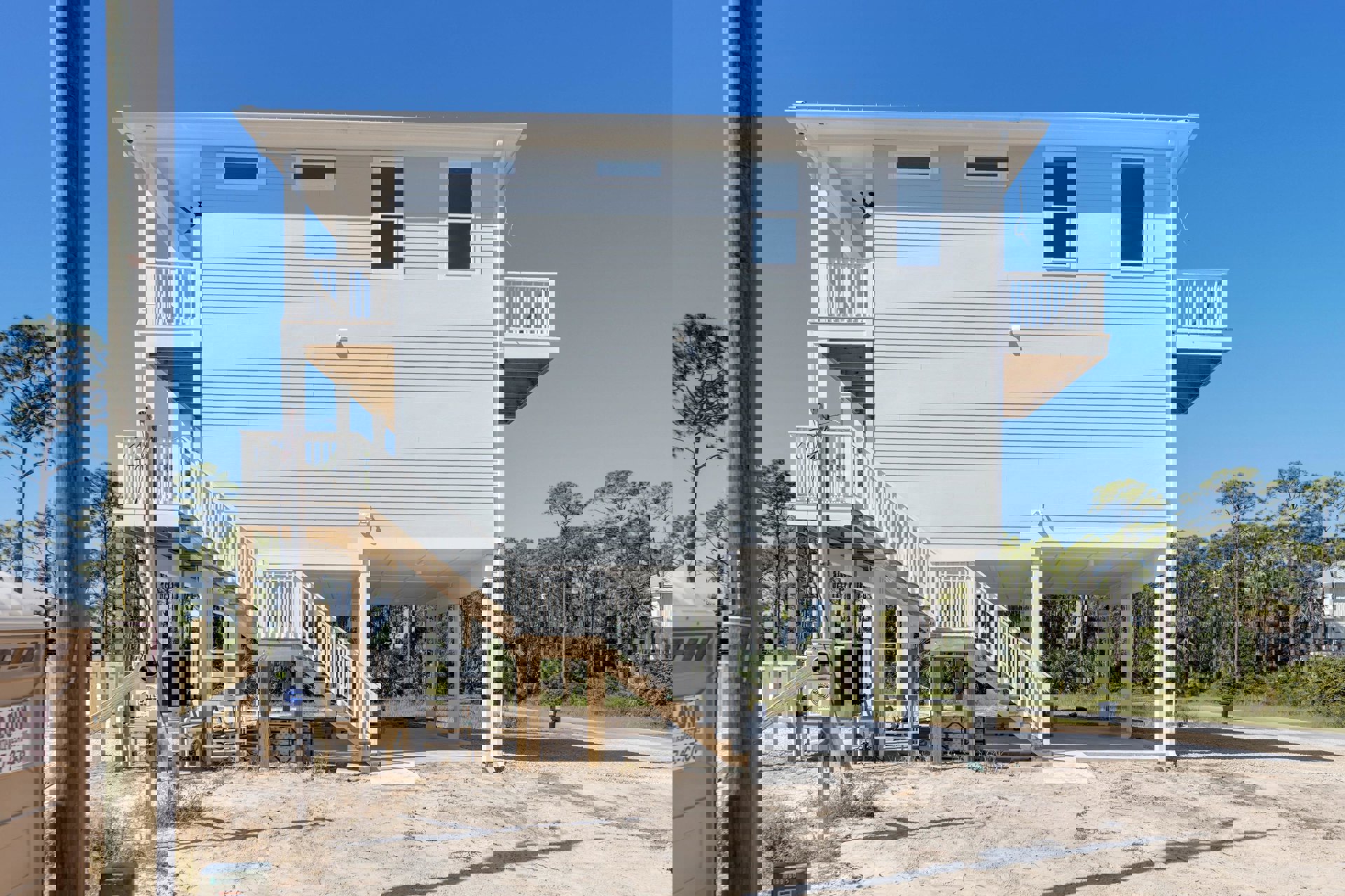 White exterior home with outdoor staircase, white-framed window, shaded porch, and surrounding trees.