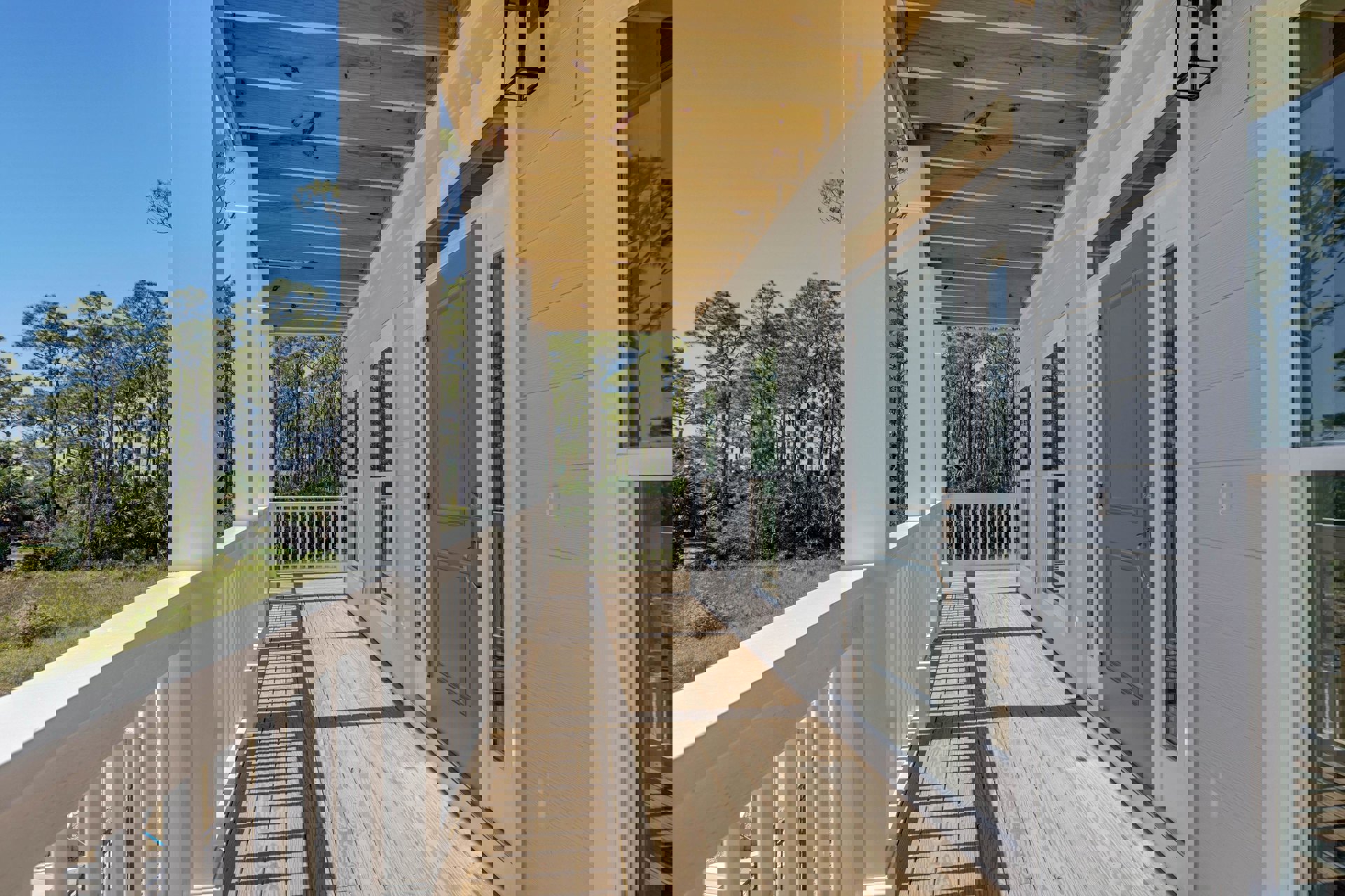 Grey front door framed by white porch railing, surrounded by leafy trees and bushes, outdoor deck area with baluster details