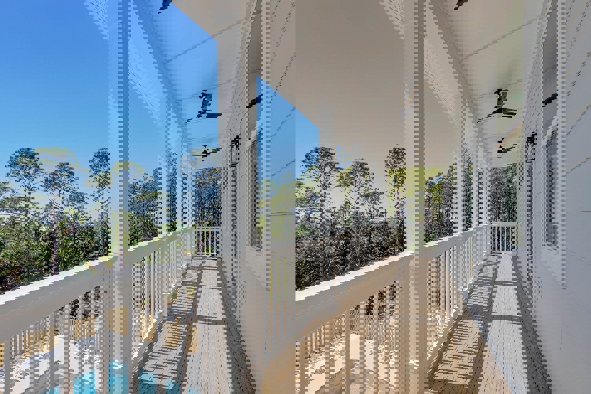 Spacious deck with white railings overlooking a rectangular pool, surrounded by mature trees and lush greenery