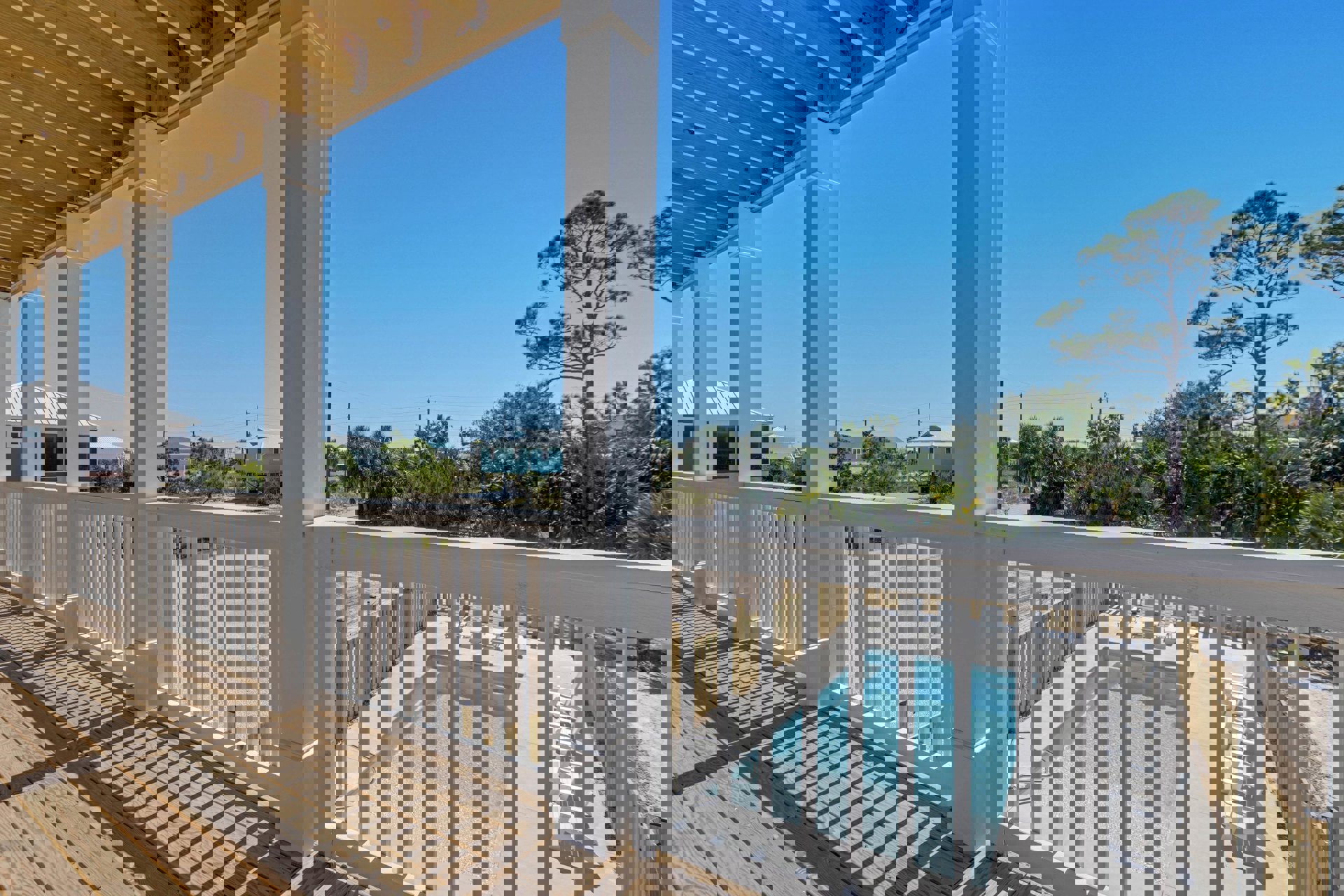 Wooden deck with white railing overlooking a rectangular pool, surrounded by leafy trees and a fence, outdoor chair in foreground