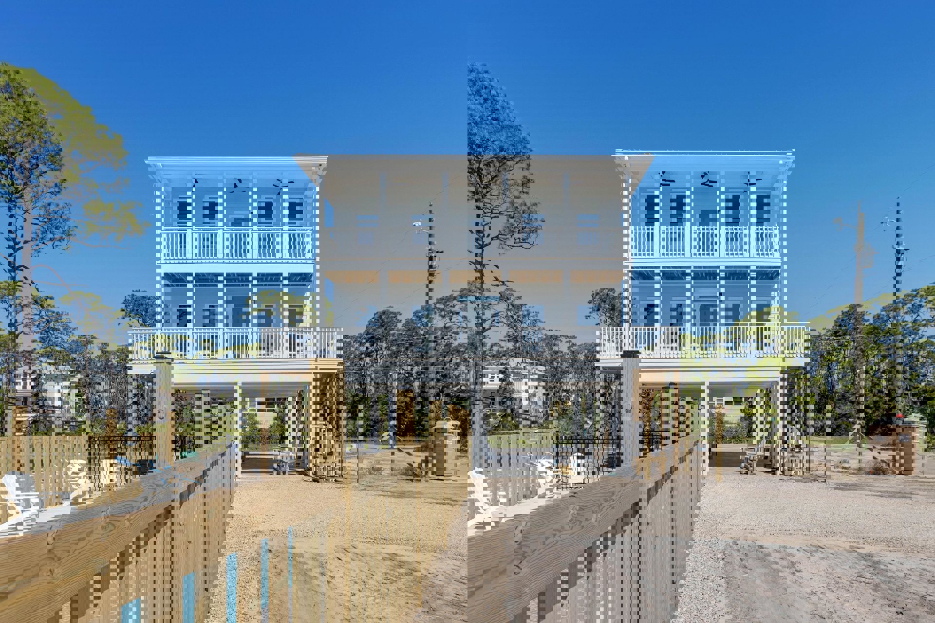 White two-story house with balcony, wood and metal fencing, outdoor seating area, swimming pool, and mature tree in landscaped yard.