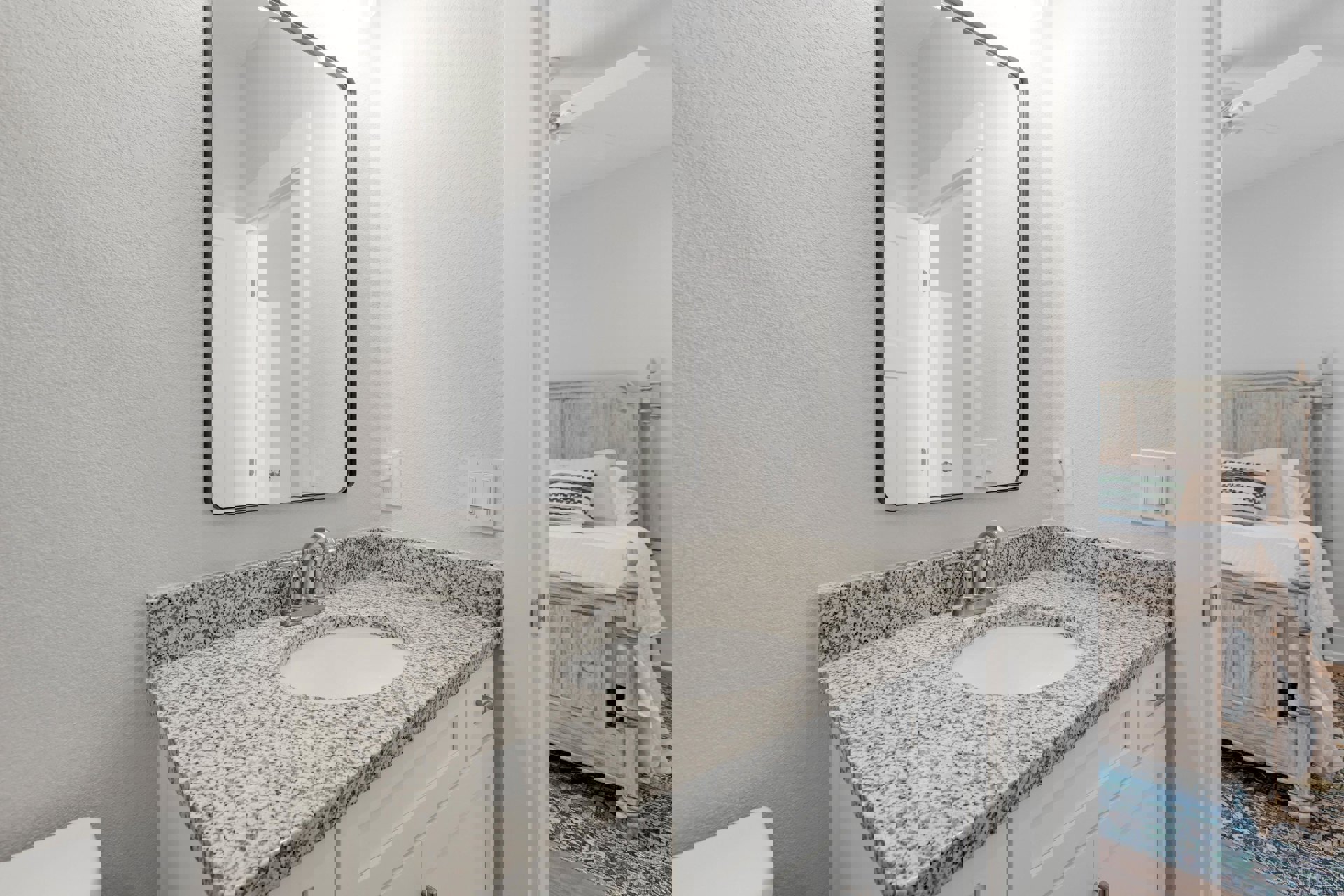 White bathroom vanity with black speckled countertop, undermount sink, chrome faucet, large wall mirror, and tiled backsplash