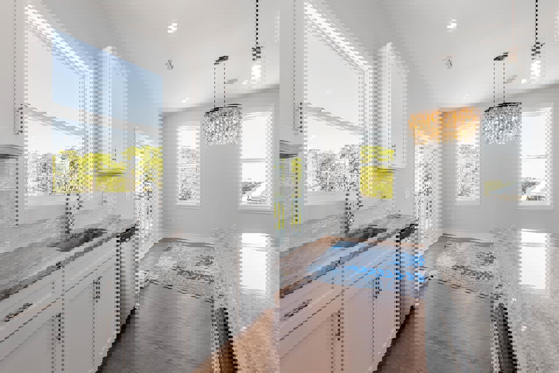 Marble countertops, blue rug on hardwood floor, silver refrigerator, modern chandelier, white cabinetry, stainless steel faucet, large window with trees visible outside