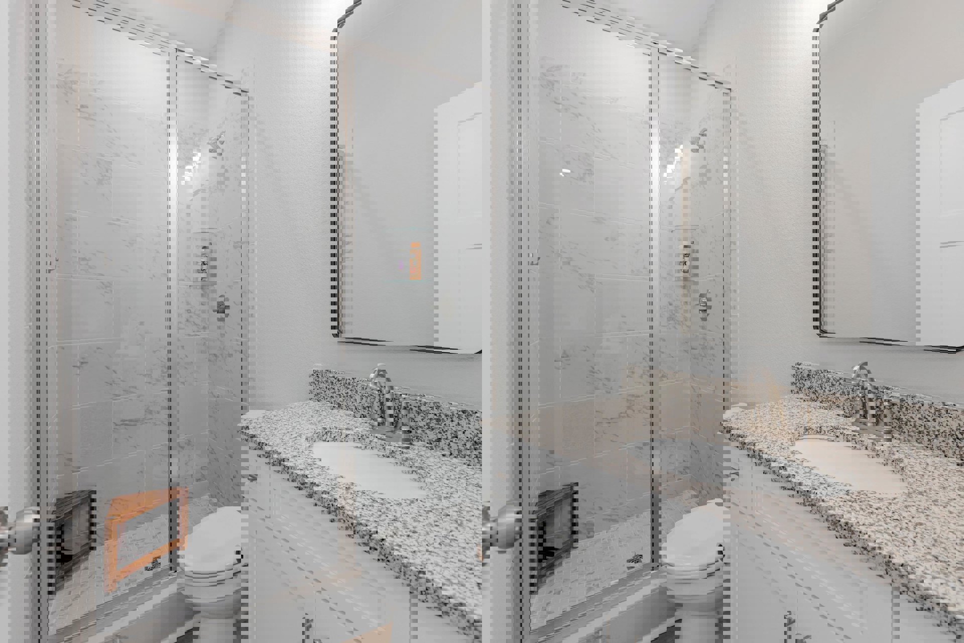 Bathroom with tiled shower, wooden corner bench, white toilet, stone countertop with sink, wall-mounted mirror, and chrome fixtures