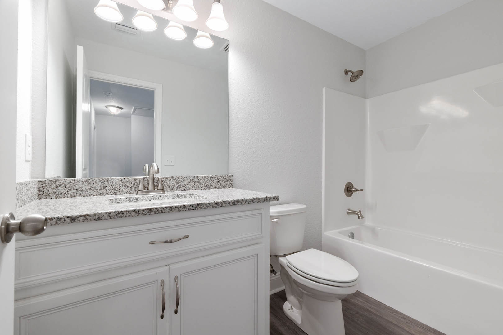 Modern bathroom featuring white tile walls, a rectangular vanity with undermount sink, chrome faucet, closed toilet, freestanding bathtub, brushed metal shower head, and recessed