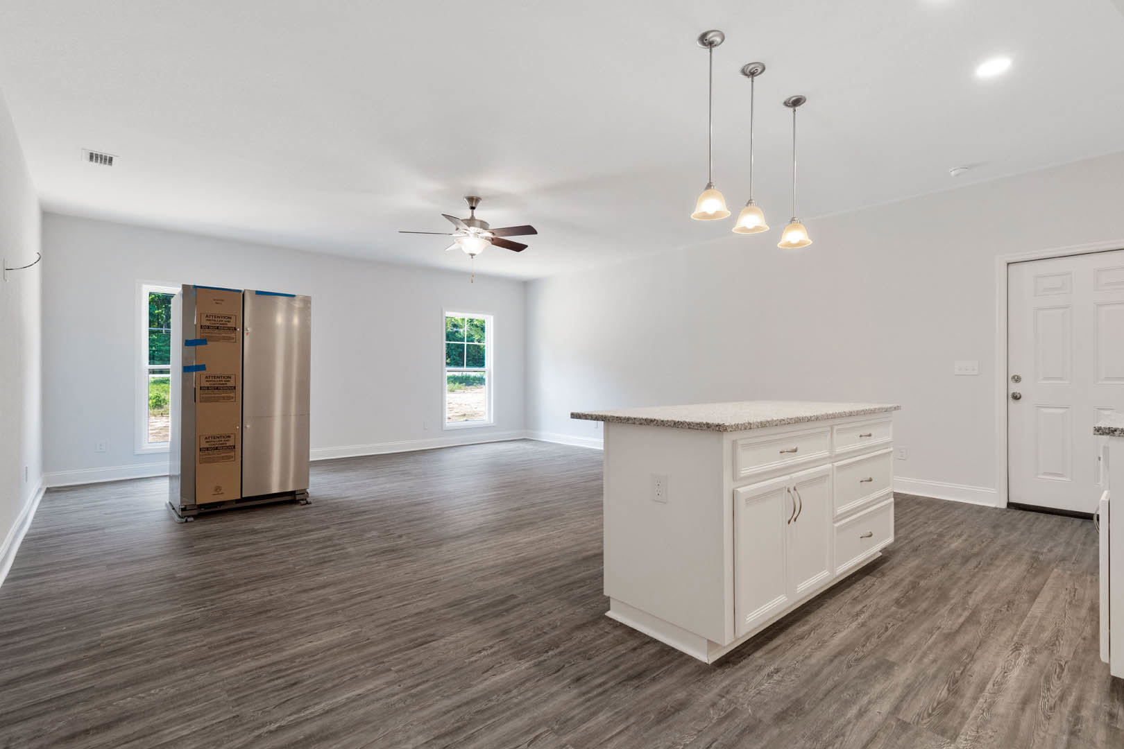 Kitchen with wood flooring, white cabinetry, central island with drawers, ceiling fan with light, white door with silver handle, and window framed in white