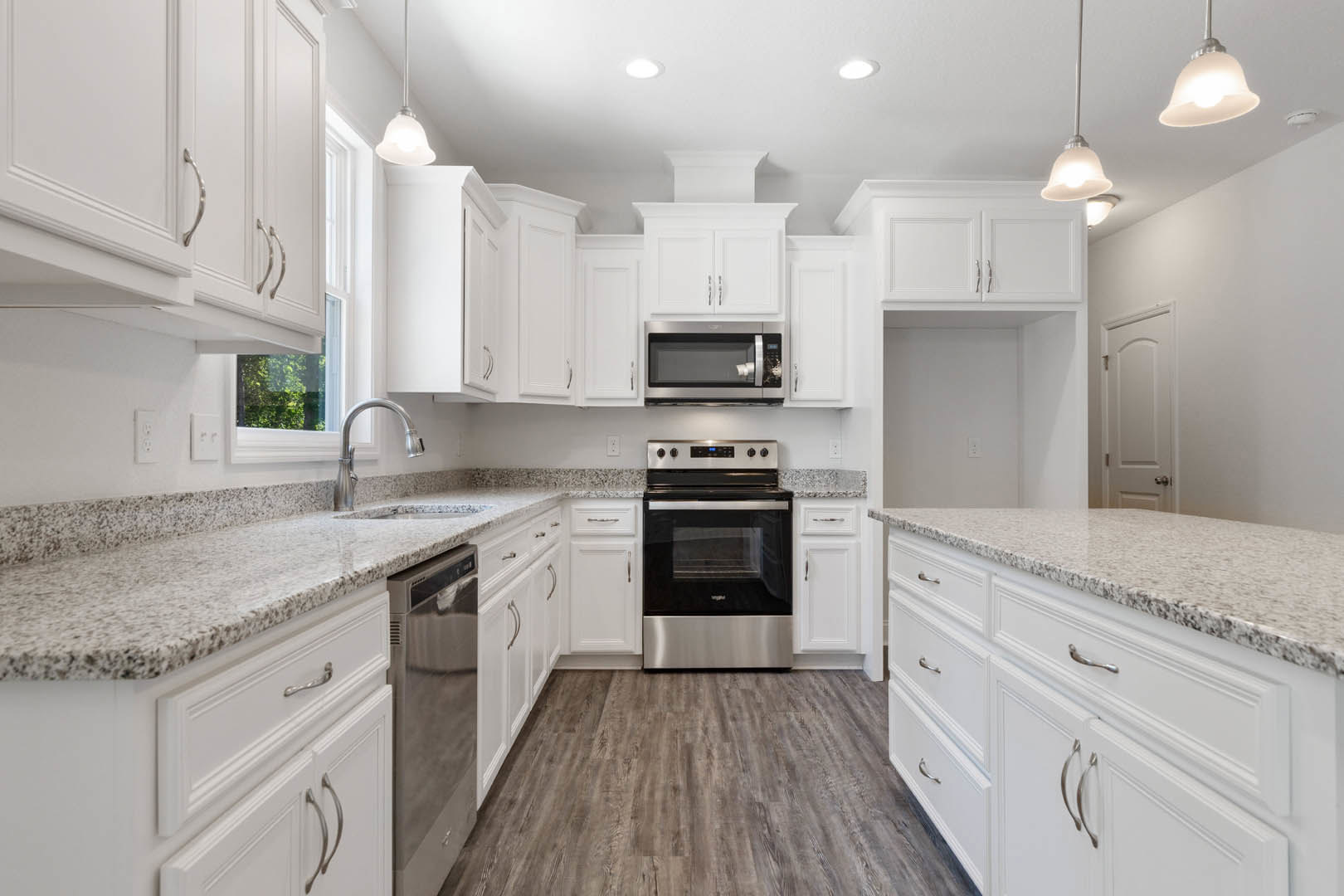 White kitchen cabinets with granite countertops, stainless steel refrigerator, wood flooring, built-in stove and microwave, chrome faucet, wall mirror