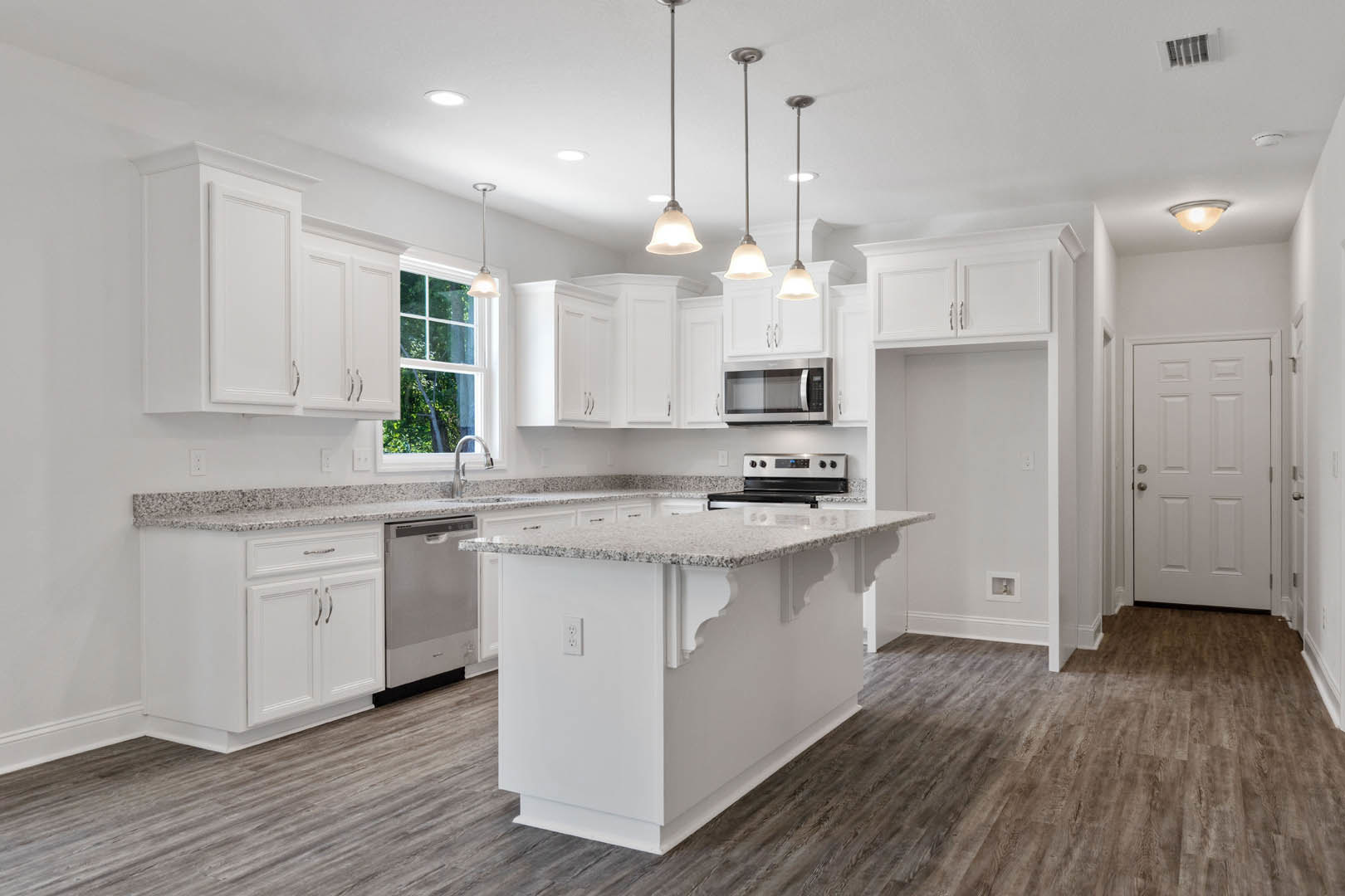 White kitchen with shaker cabinets, large central island featuring white countertop, stainless steel appliances including open microwave and stove, silver hardware, light fixture