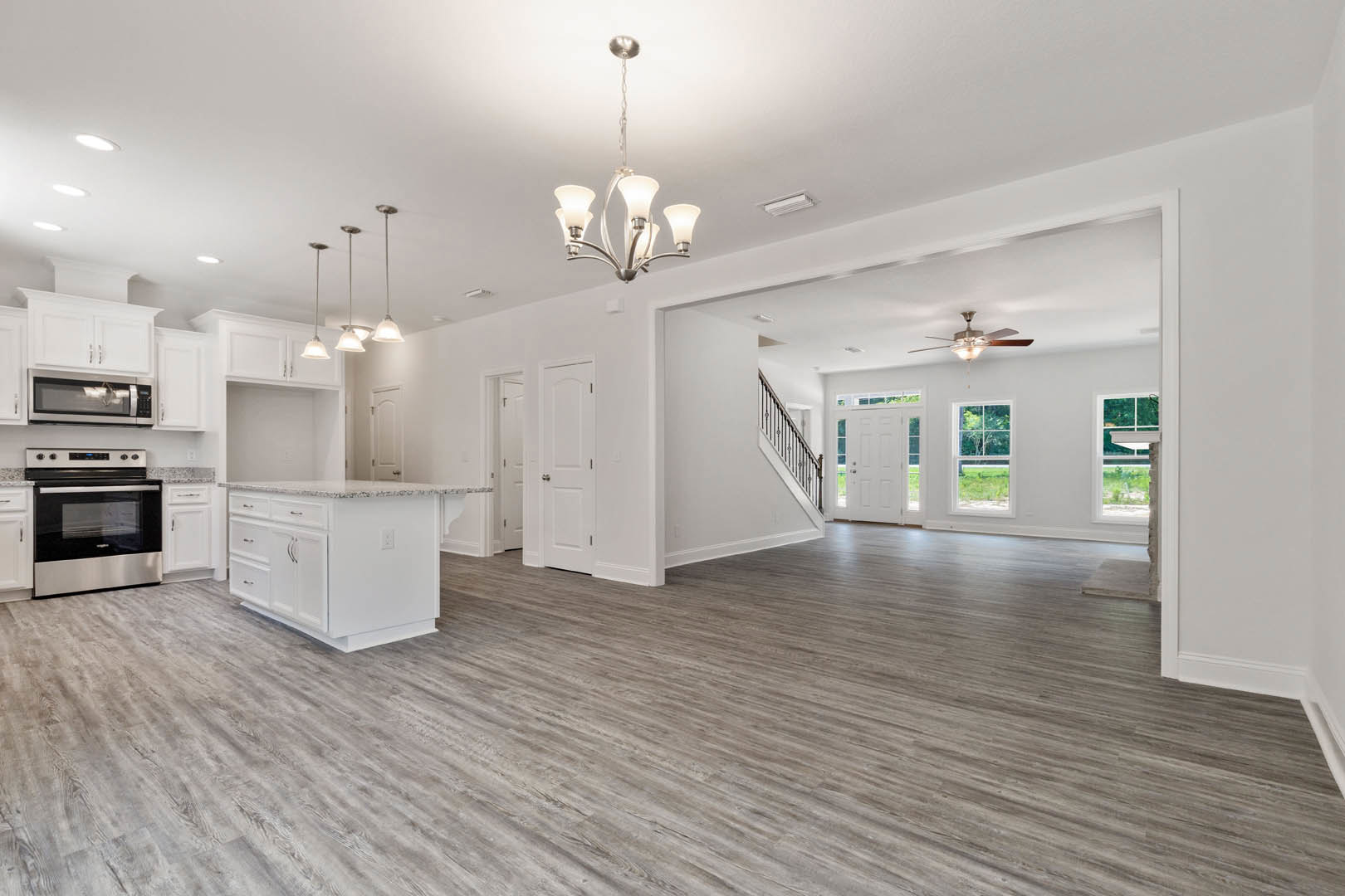 Spacious open-concept kitchen featuring a white marble-topped island, hardwood flooring, modern cabinetry, stainless steel stove, and a decorative chandelier.