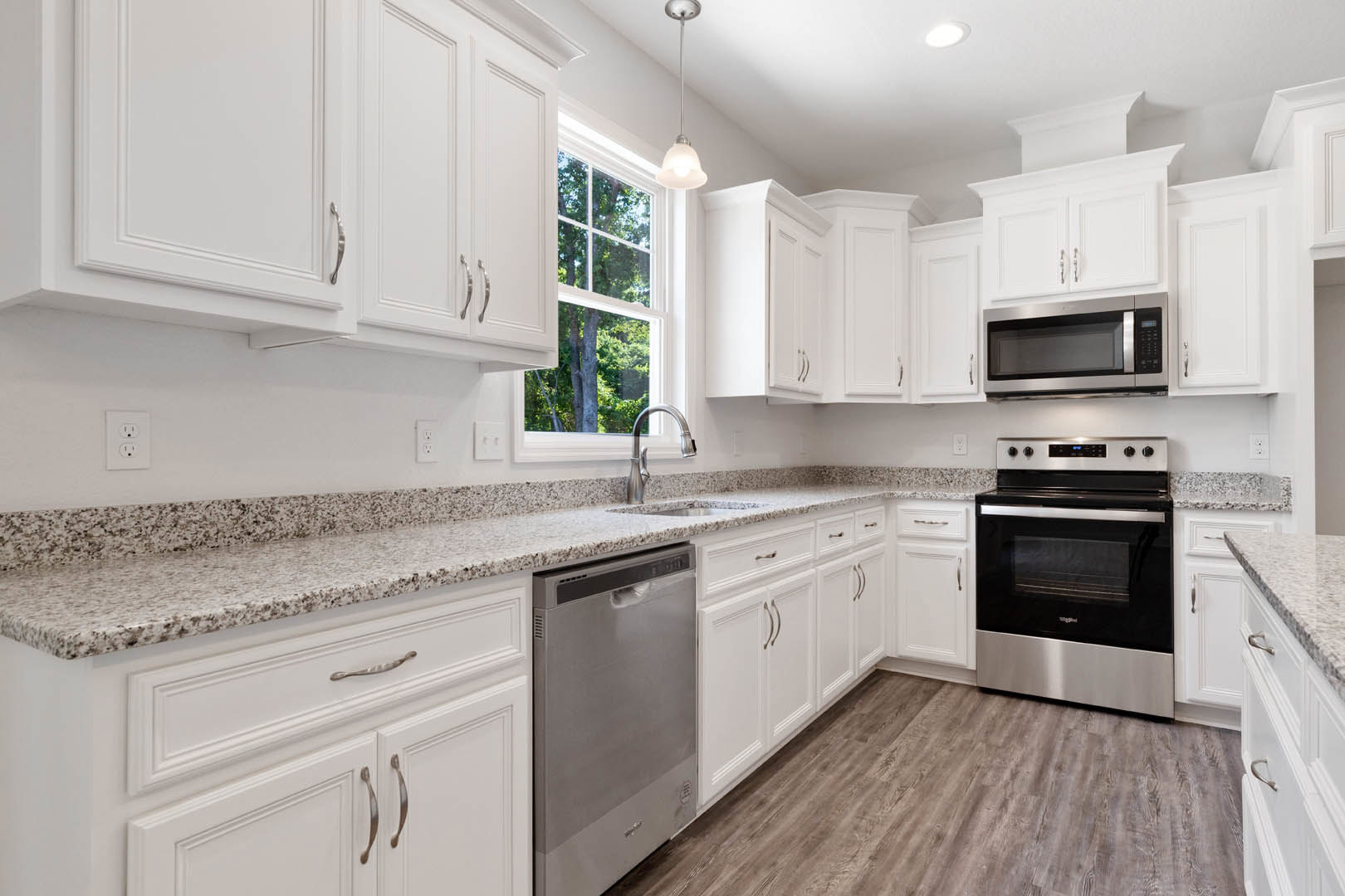 White kitchen with granite countertops, stainless steel oven and microwave, white cabinetry, chrome faucet, and ceiling light fixture.