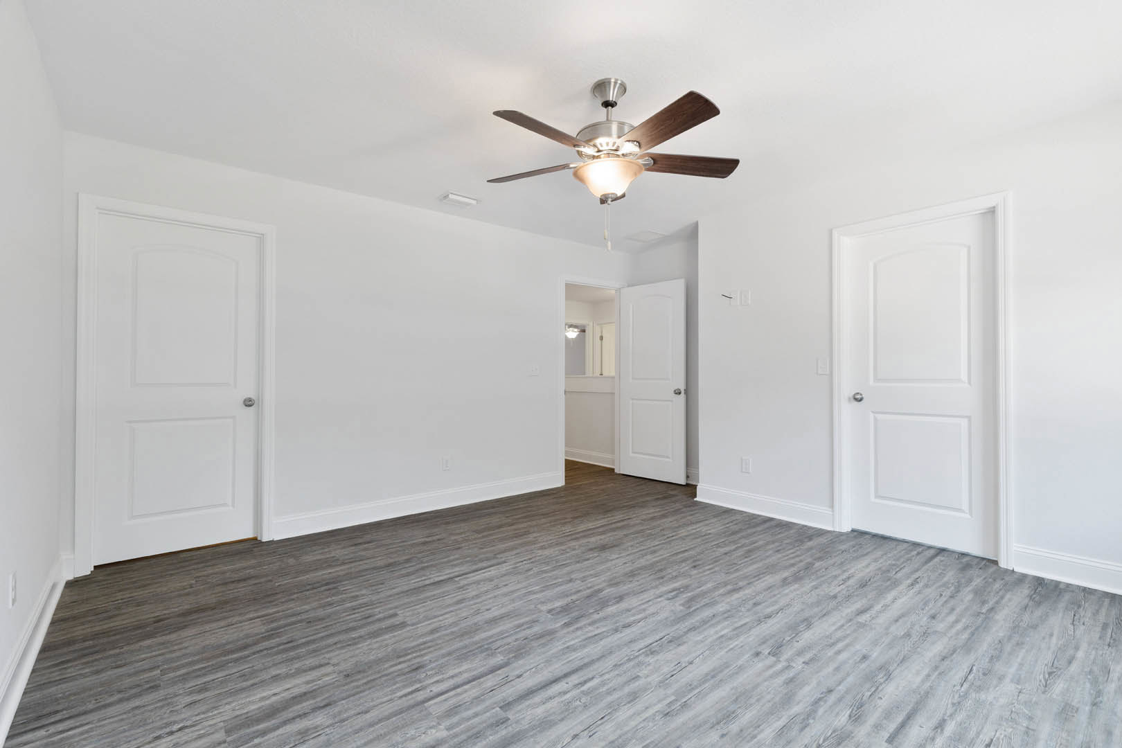 Ceiling fan with light fixture, white doors with silver handles, wood laminate flooring, white plaster walls
