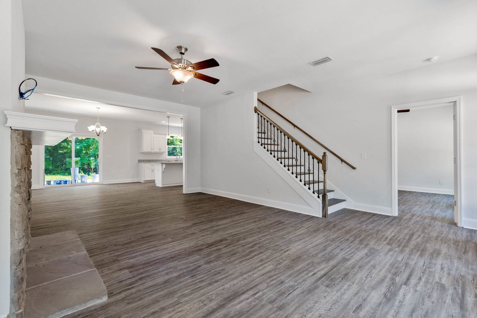 Hardwood floored room featuring a staircase with metal railings, white walls, open door, and ceiling fan with light fixture.